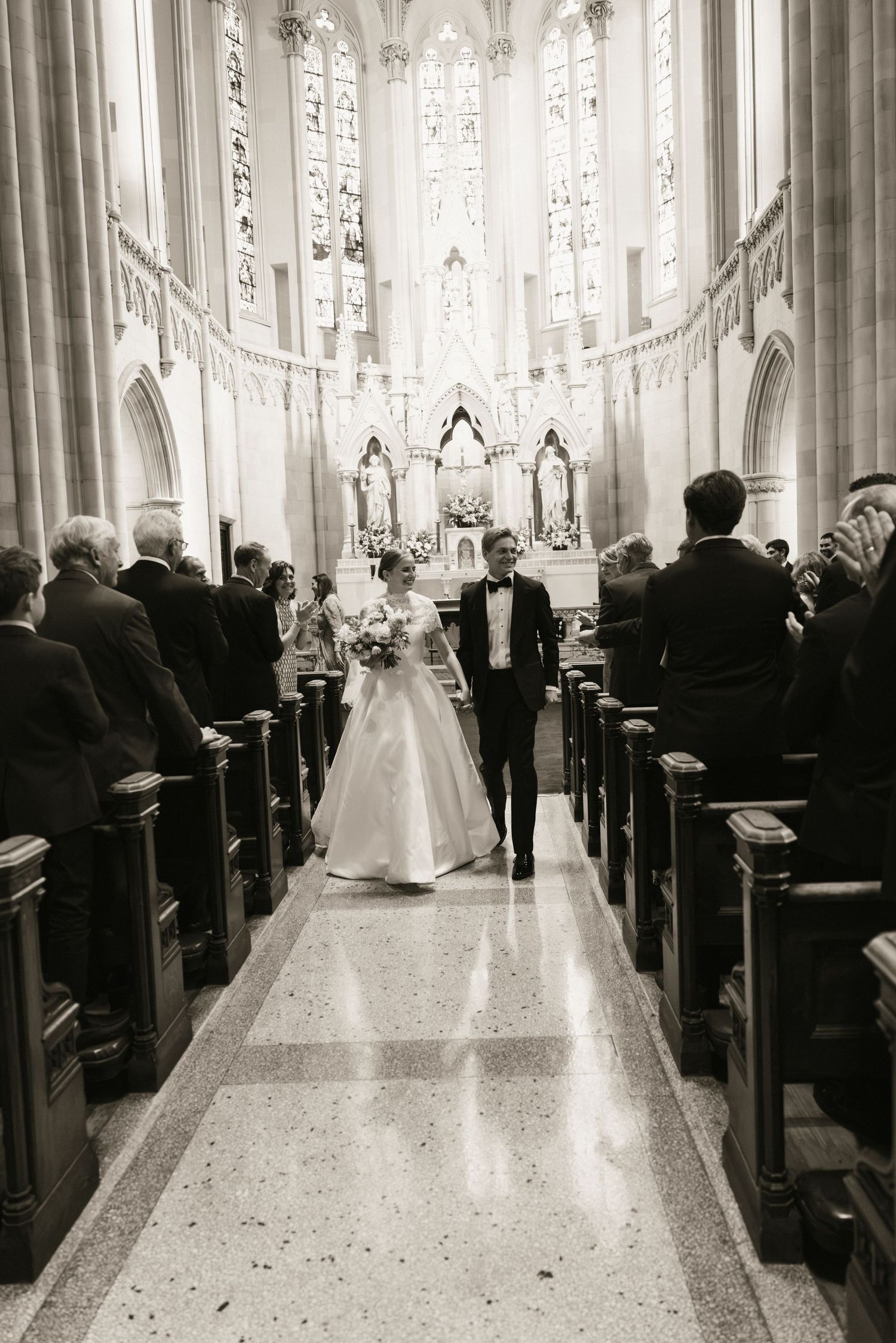 Black and white photo of newlywed couple walking down cathedral aisle after wedding ceremony.