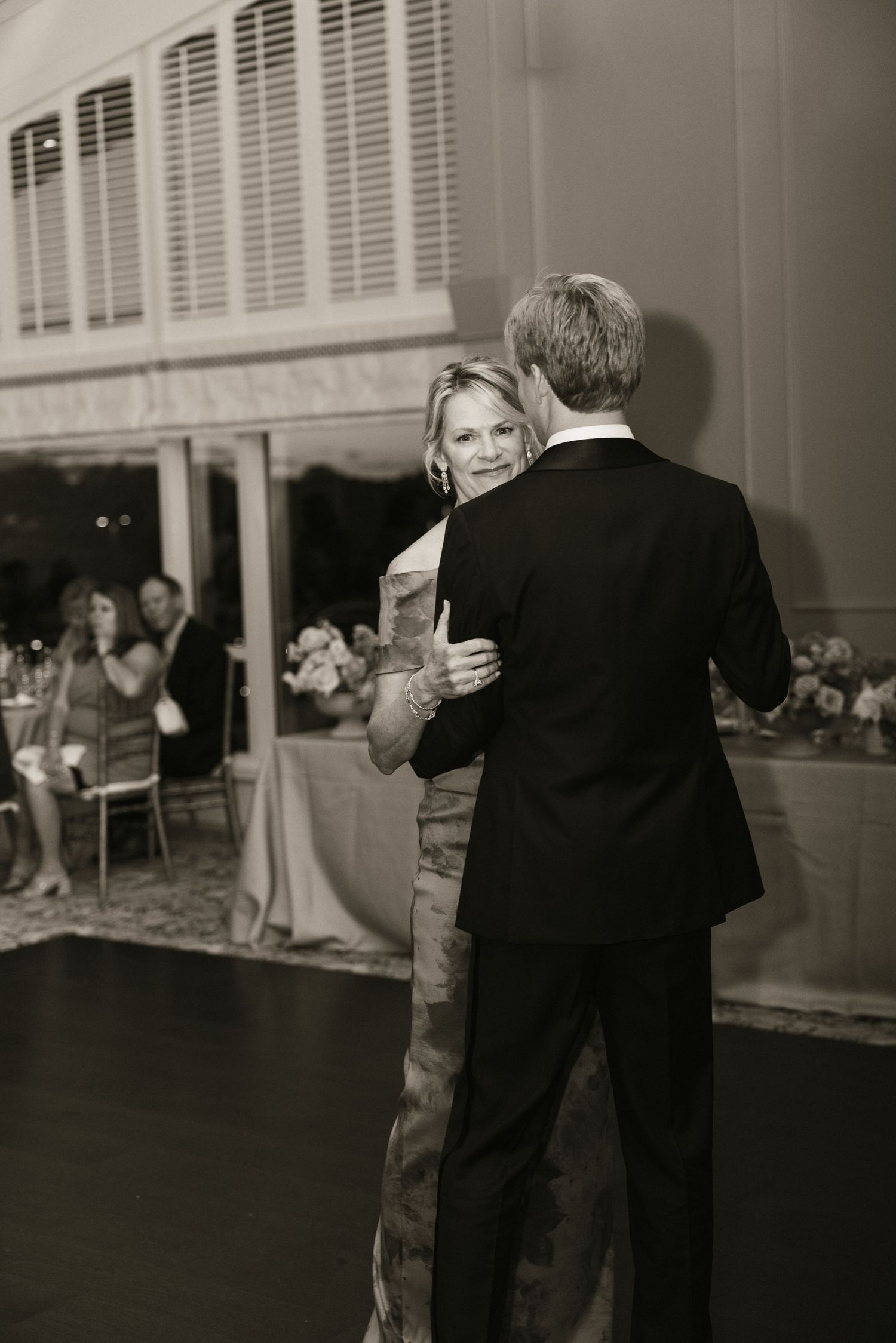 Groom shares a tender mother-son dance on the wedding reception dance floor in classic black and white photo.