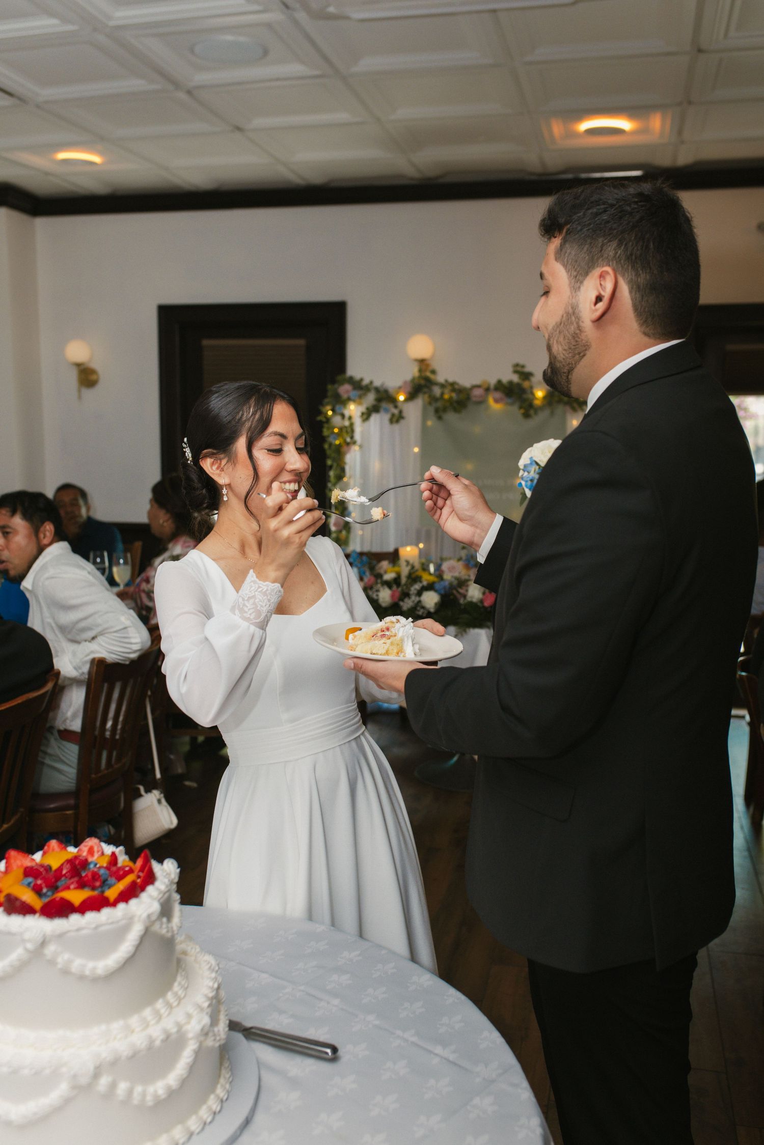 Bride and groom share wedding cake cutting moment at elegant indoor reception celebration.