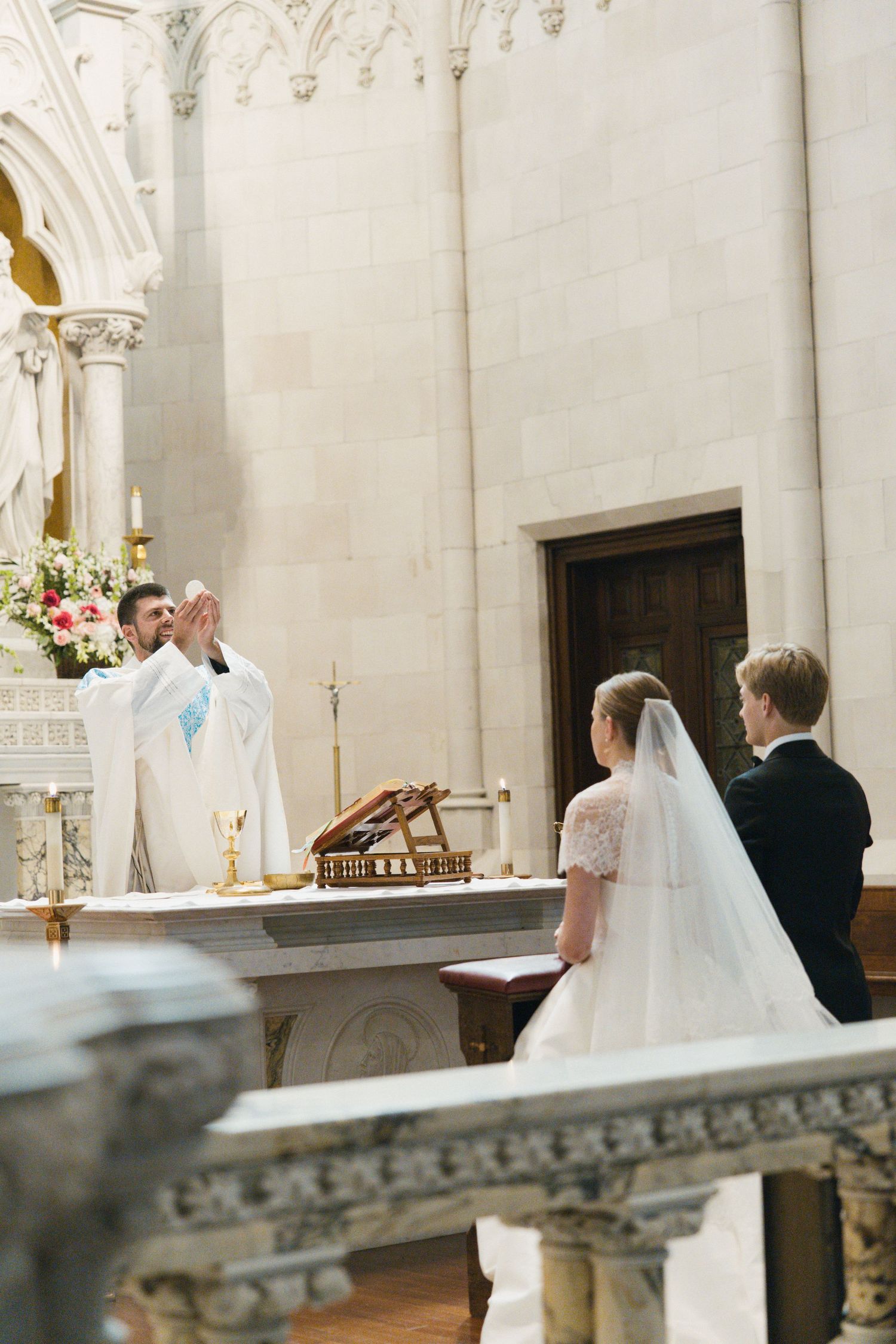Bride and groom stand before priest at marble altar during Catholic wedding ceremony in church.