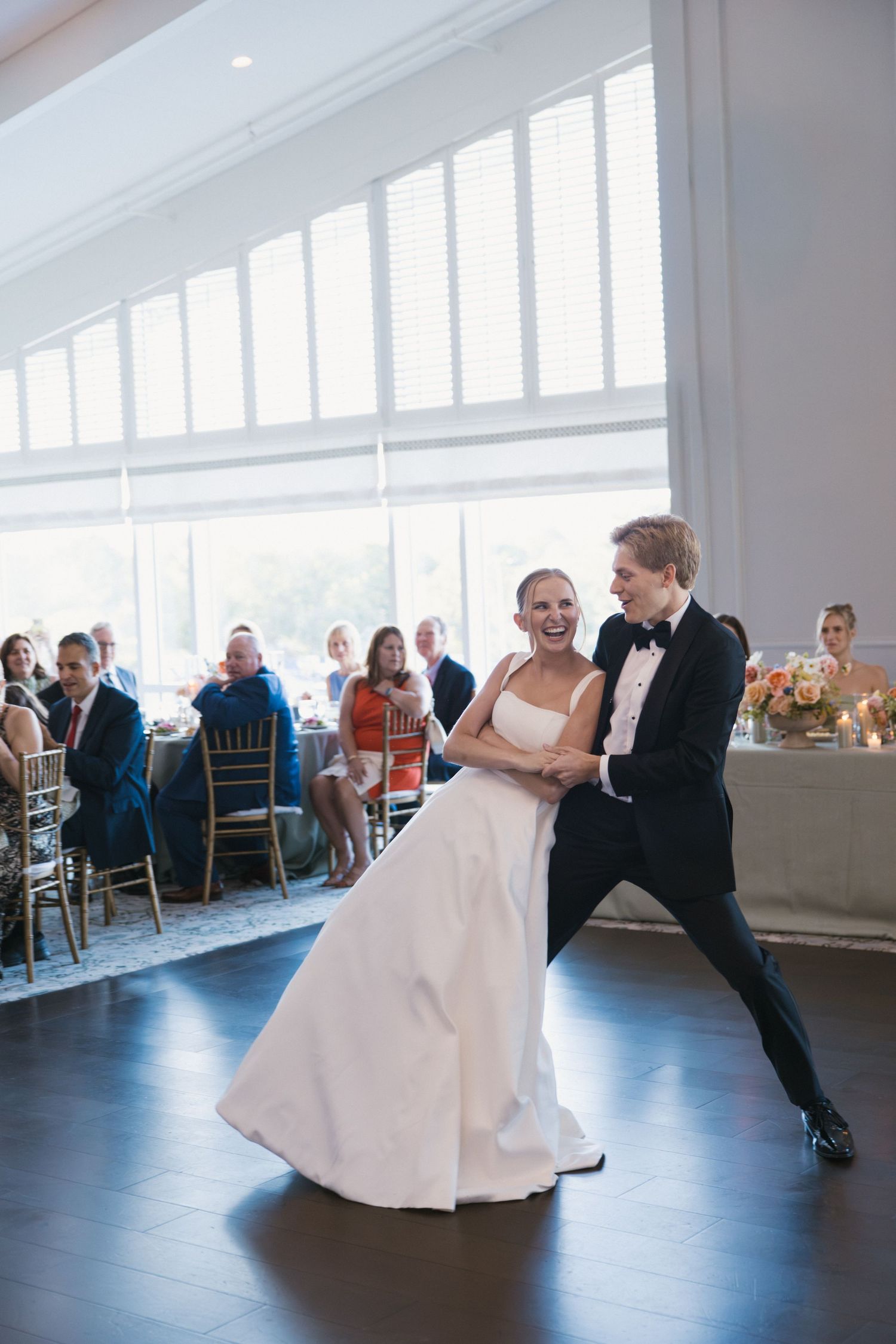 Bride and groom share their first dance at wedding reception, guests watching in elegant ballroom.