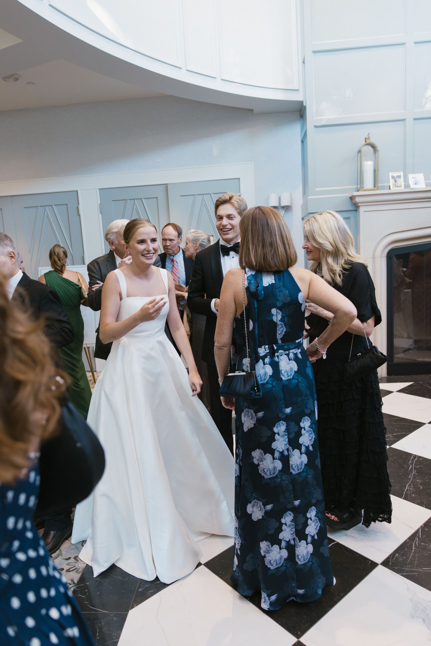 Bride in white ball gown mingles with guests in a grand reception hall with checkered floors.