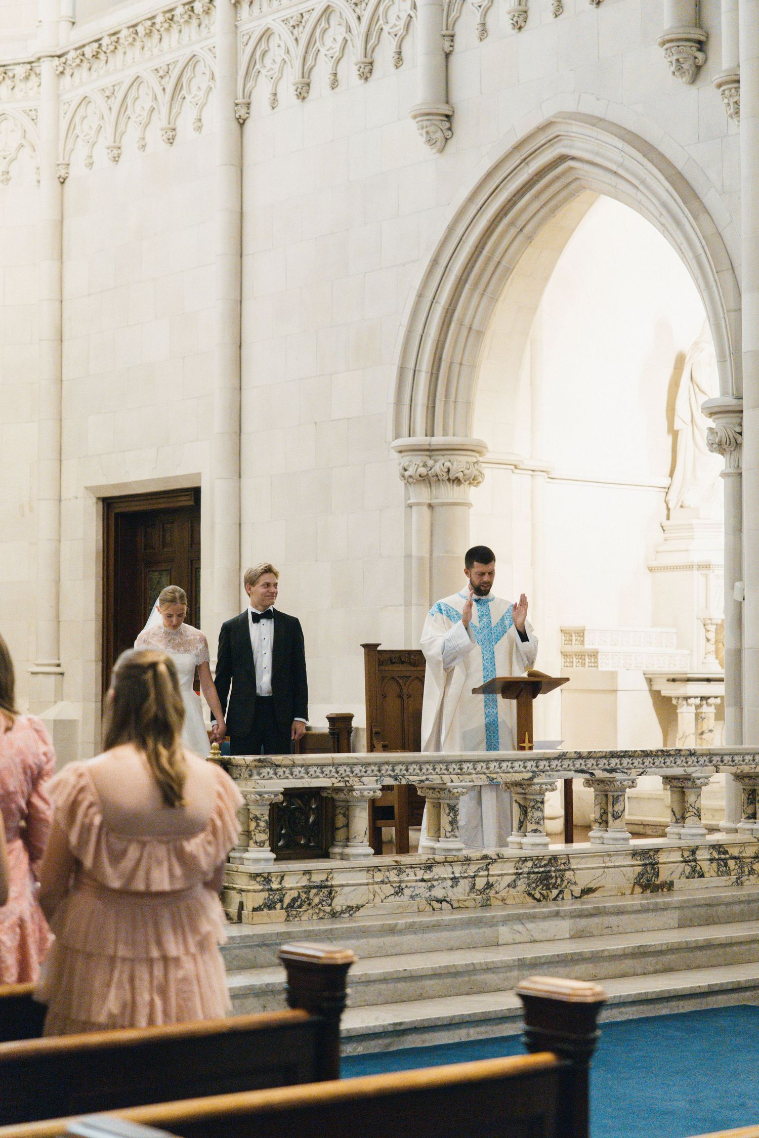 Priest officiates wedding ceremony at ornate white marble altar in elegant Gothic cathedral church.