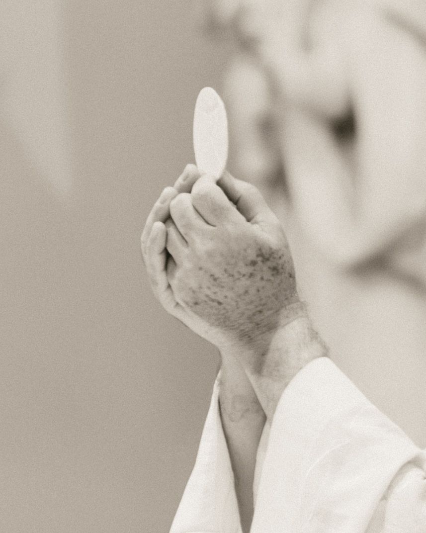 Priest holding a consecrated Eucharist host during Catholic Mass communion ceremony in white vestments.