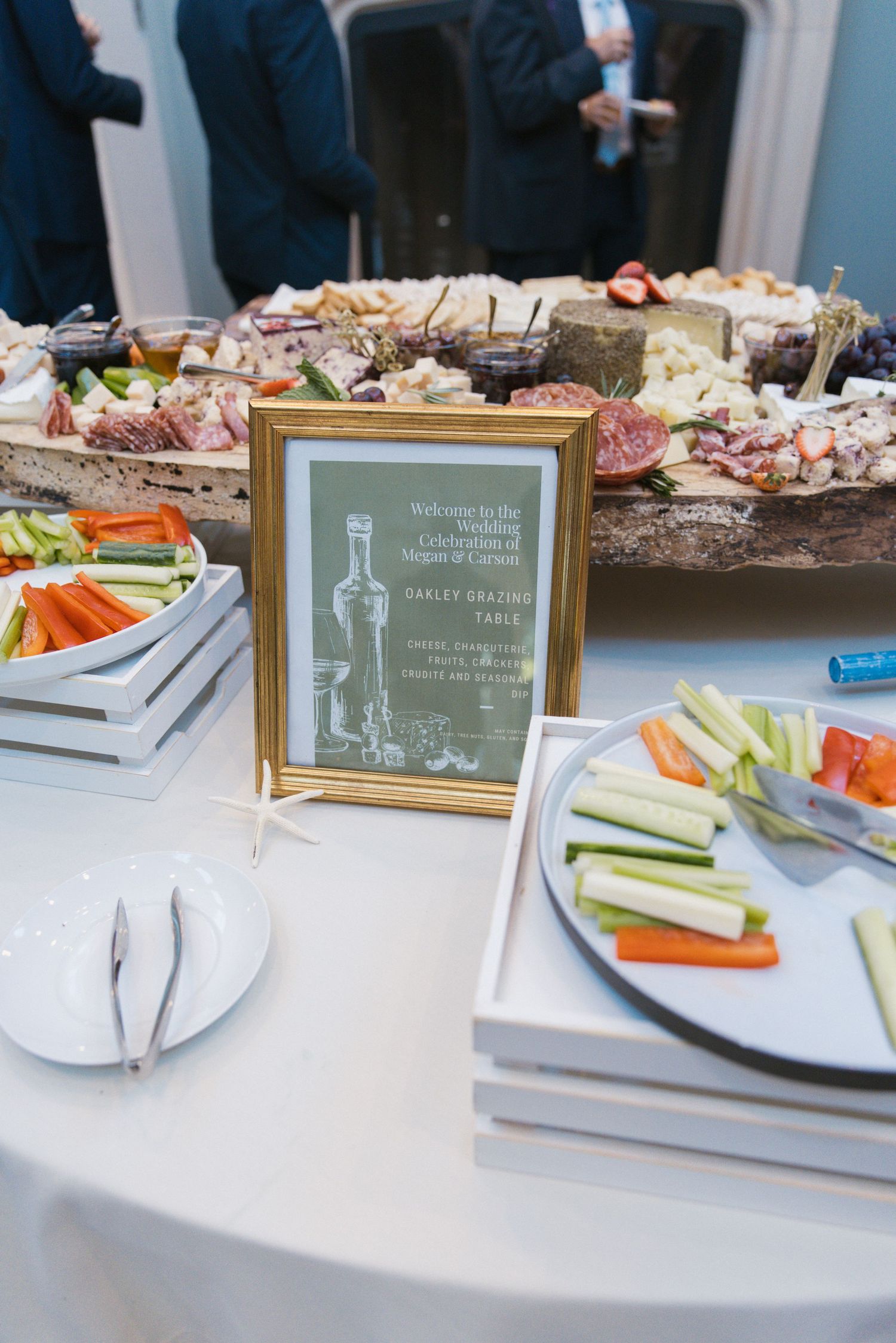 Wedding grazing table display with charcuterie, vegetables, and framed Oakley Grazing Table sign.