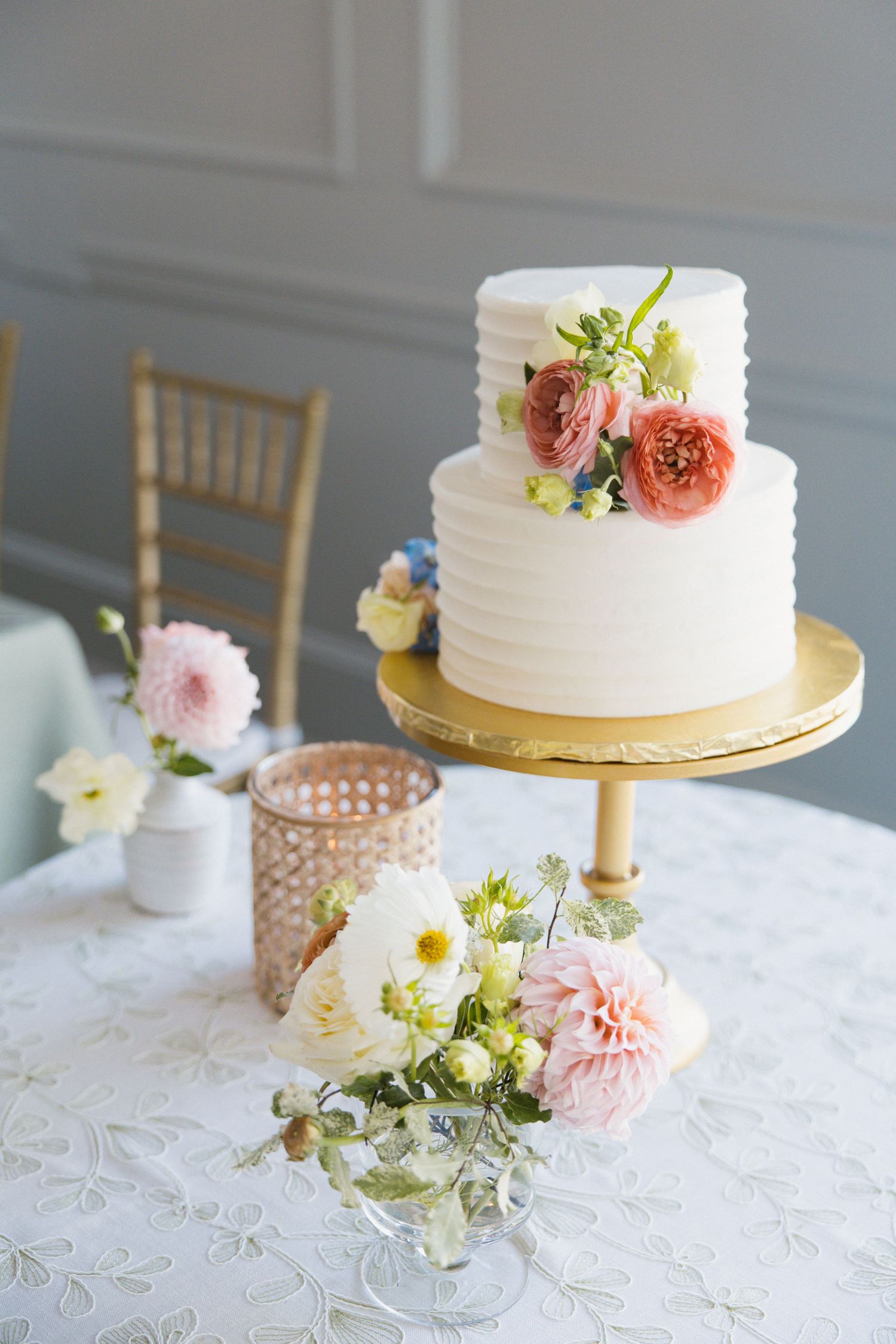 Elegant two-tier white textured wedding cake with pink and peach flowers on a gold cake stand.