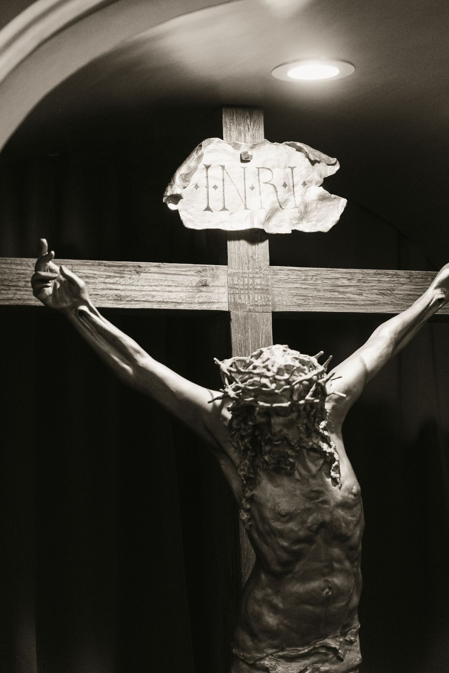 Black and white close-up of Jesus Christ crucifixion statue with INRI inscription on wooden cross.