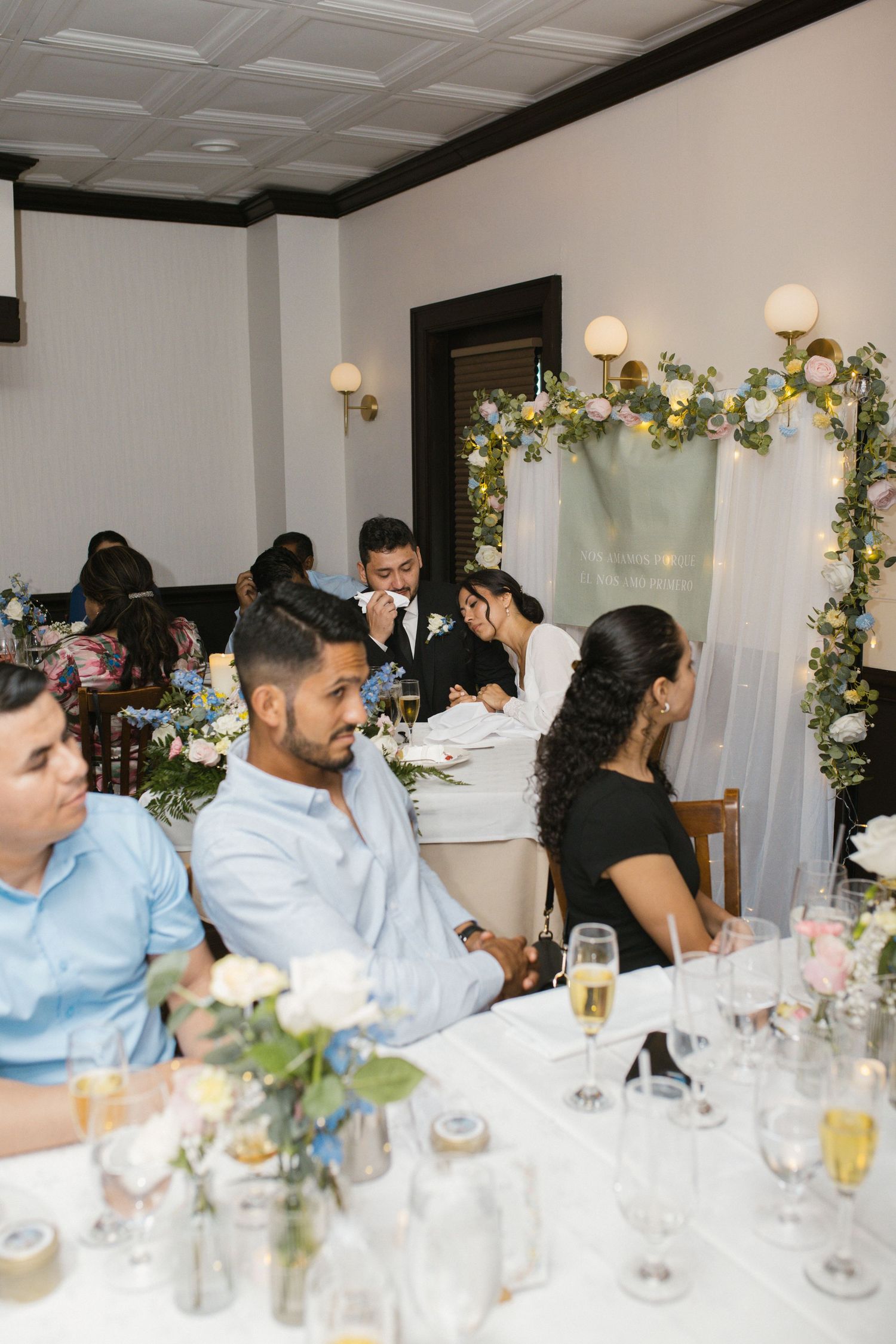 Wedding reception guests seated at decorated tables with floral centerpieces and champagne glasses.