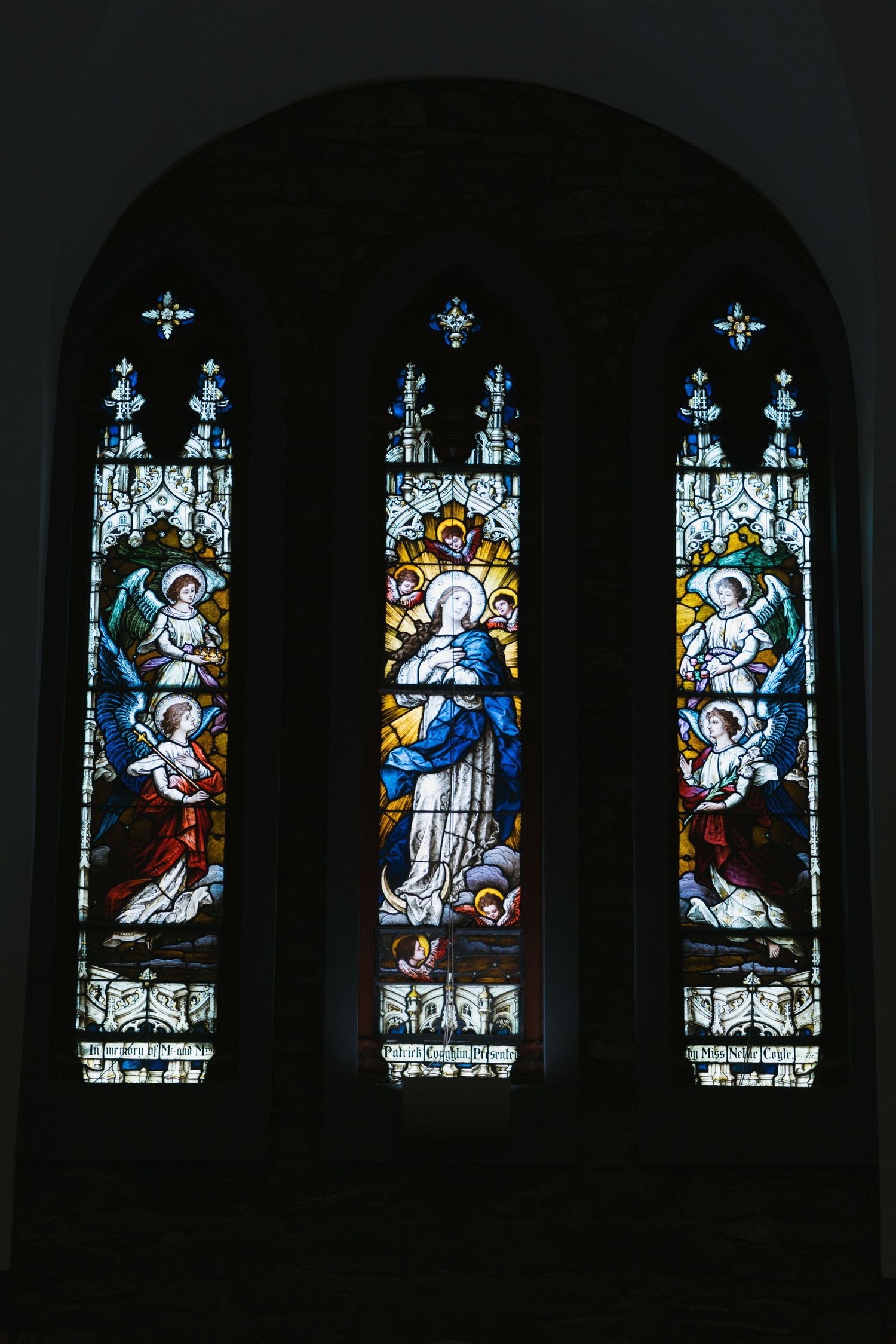 Beautiful stained glass church window depicting Virgin Mary surrounded by angels in colorful detail.