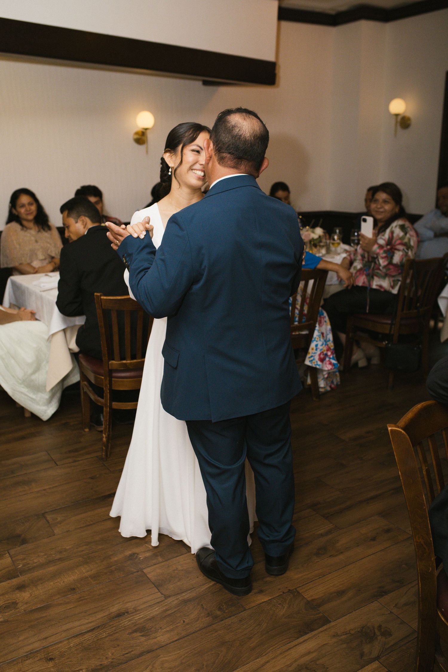 Smiling bride in white gown dancing with groom in navy suit at wedding reception.