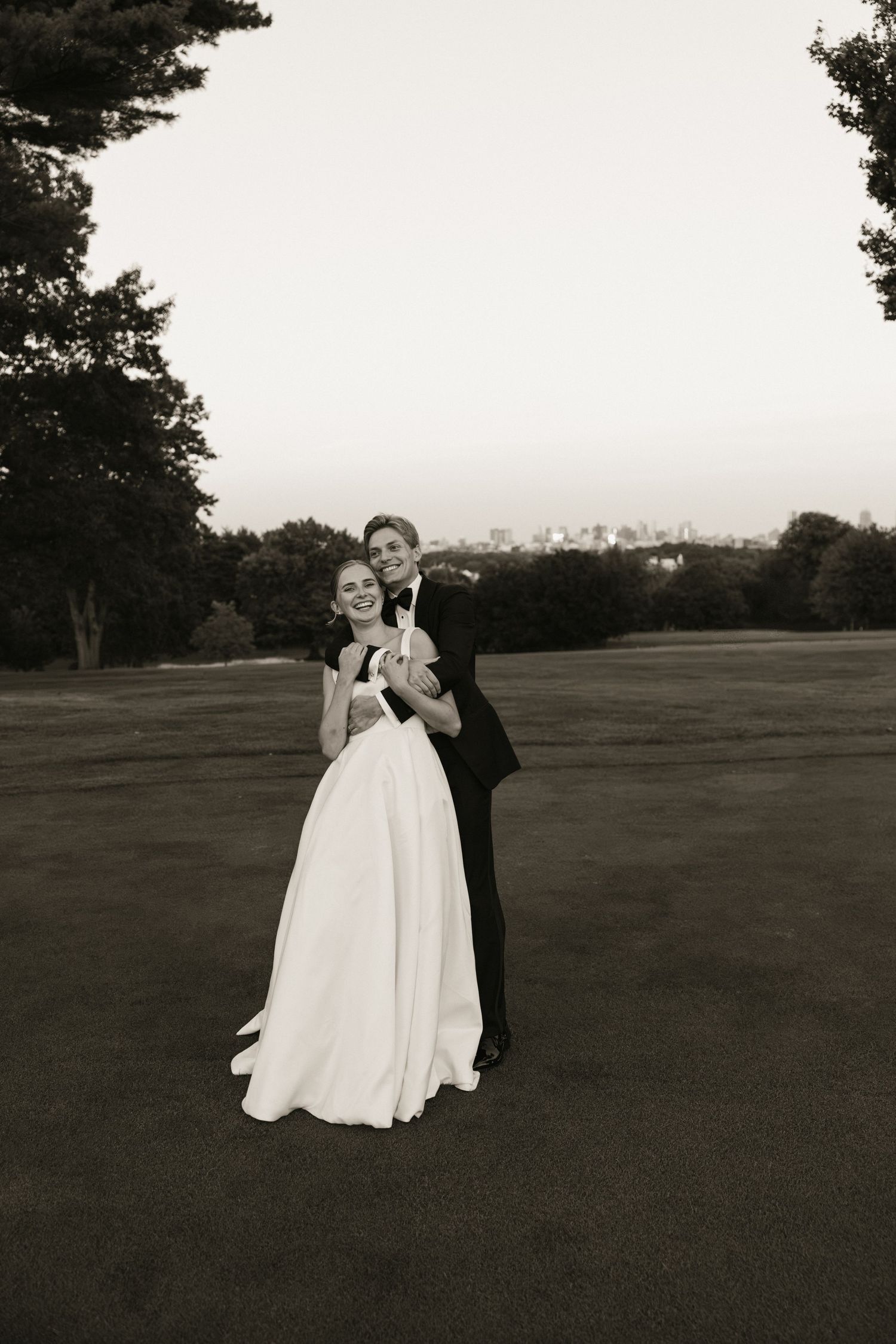 Bride and groom embracing on a golf course at dusk in a classic black and white wedding photo.