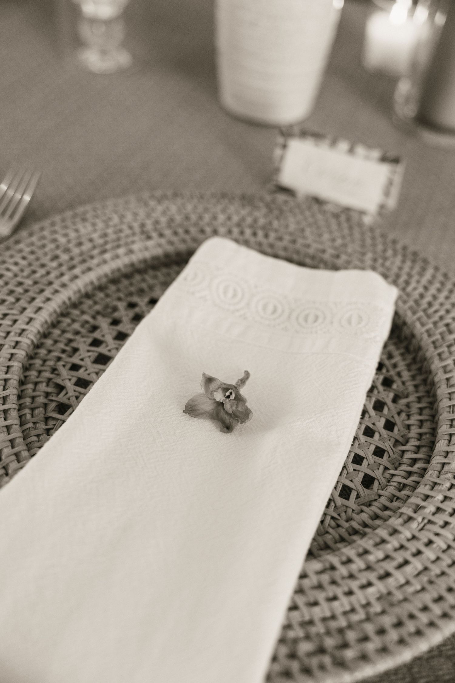 Elegant black and white wedding place setting with woven charger plate and floral napkin accent.