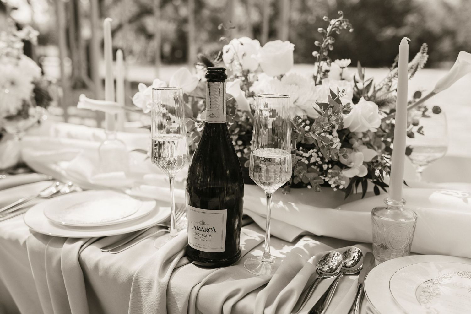 Catholic Black and white wedding reception table setting with champagne bottle, floral centerpiece, and elegant glassware.