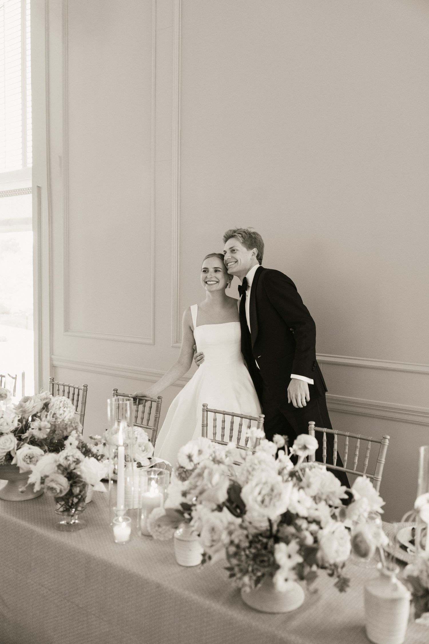 Bride and groom stand together smiling at their elegant wedding reception with floral centerpieces in black and white.