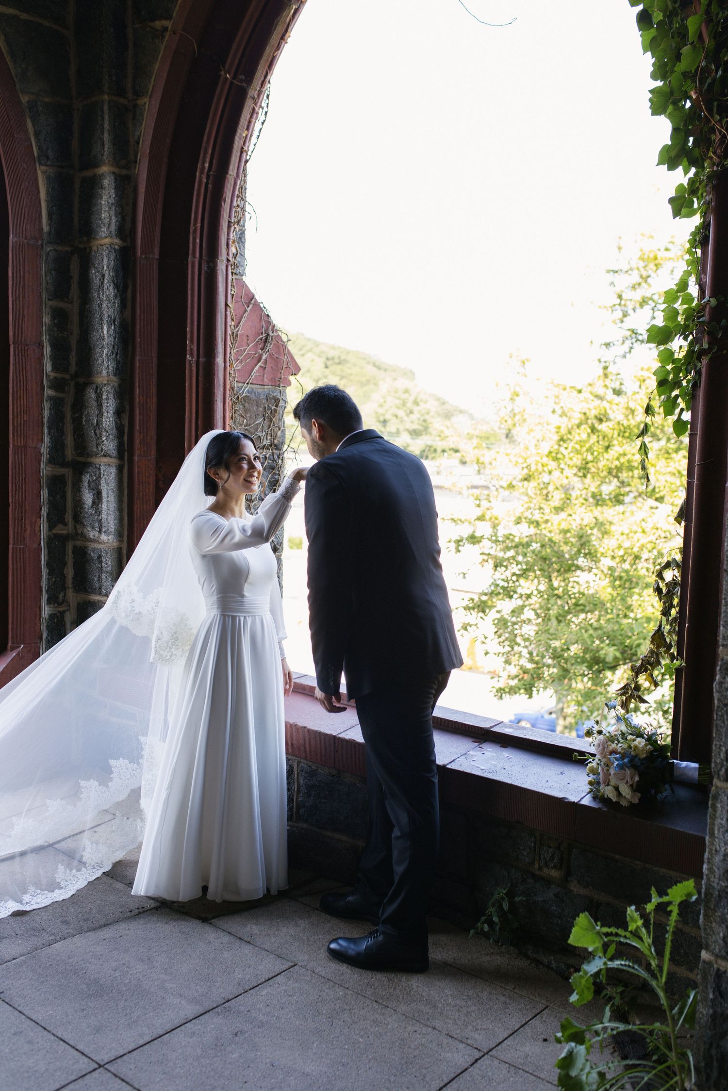 Bride and groom share a tender moment in a stone church archway, bride wearing a flowing white gown and veil.