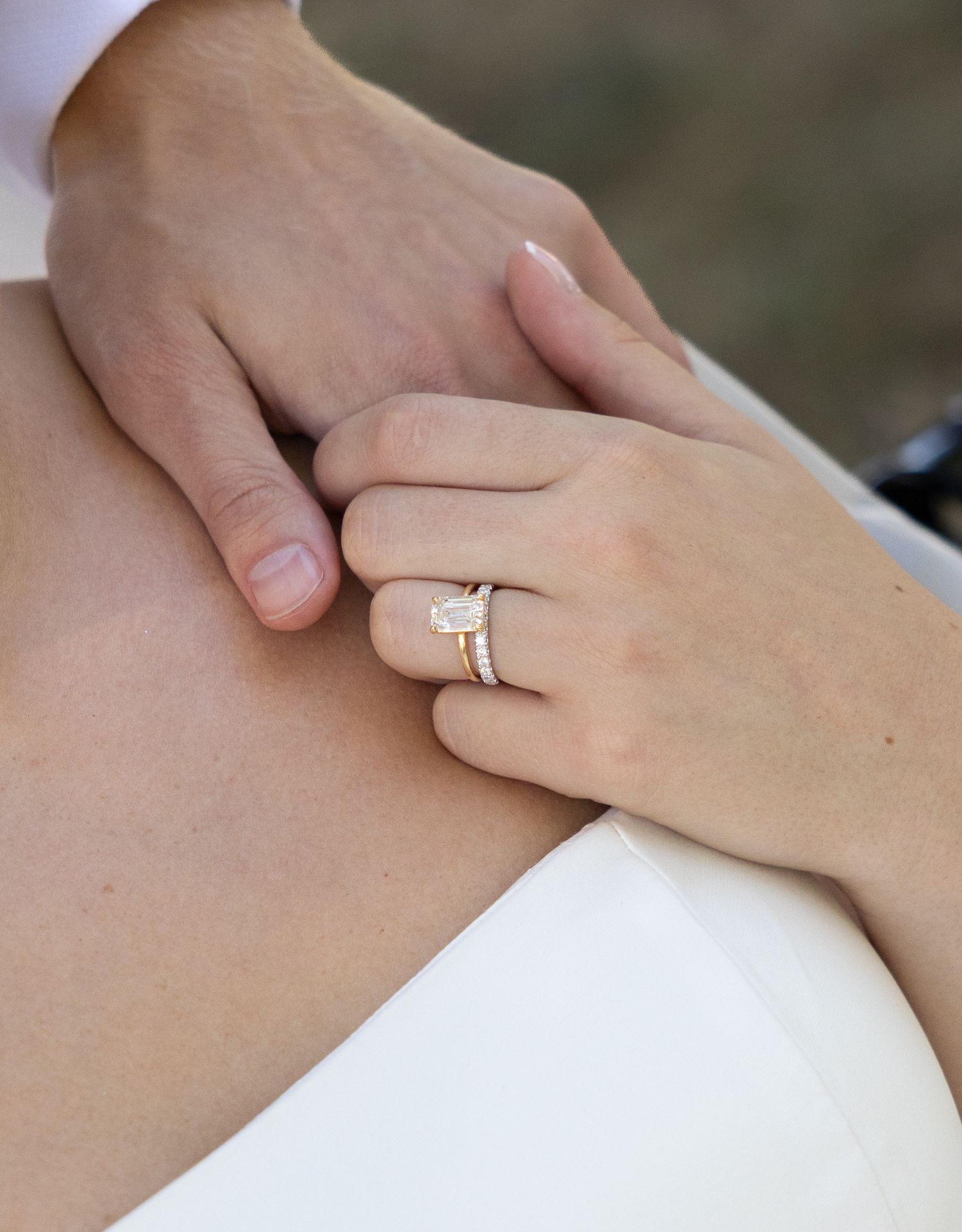 Close-up of a woman's hand wearing a stunning emerald-cut diamond engagement ring with gold wedding band.
