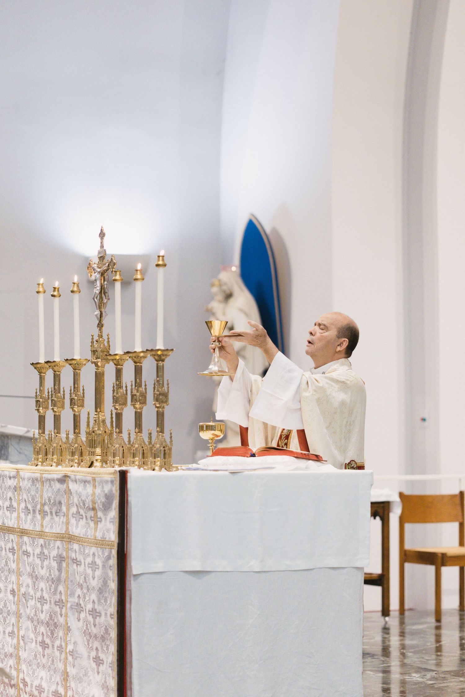Catholic priest elevating the chalice during Mass at a decorated altar with candelabras.