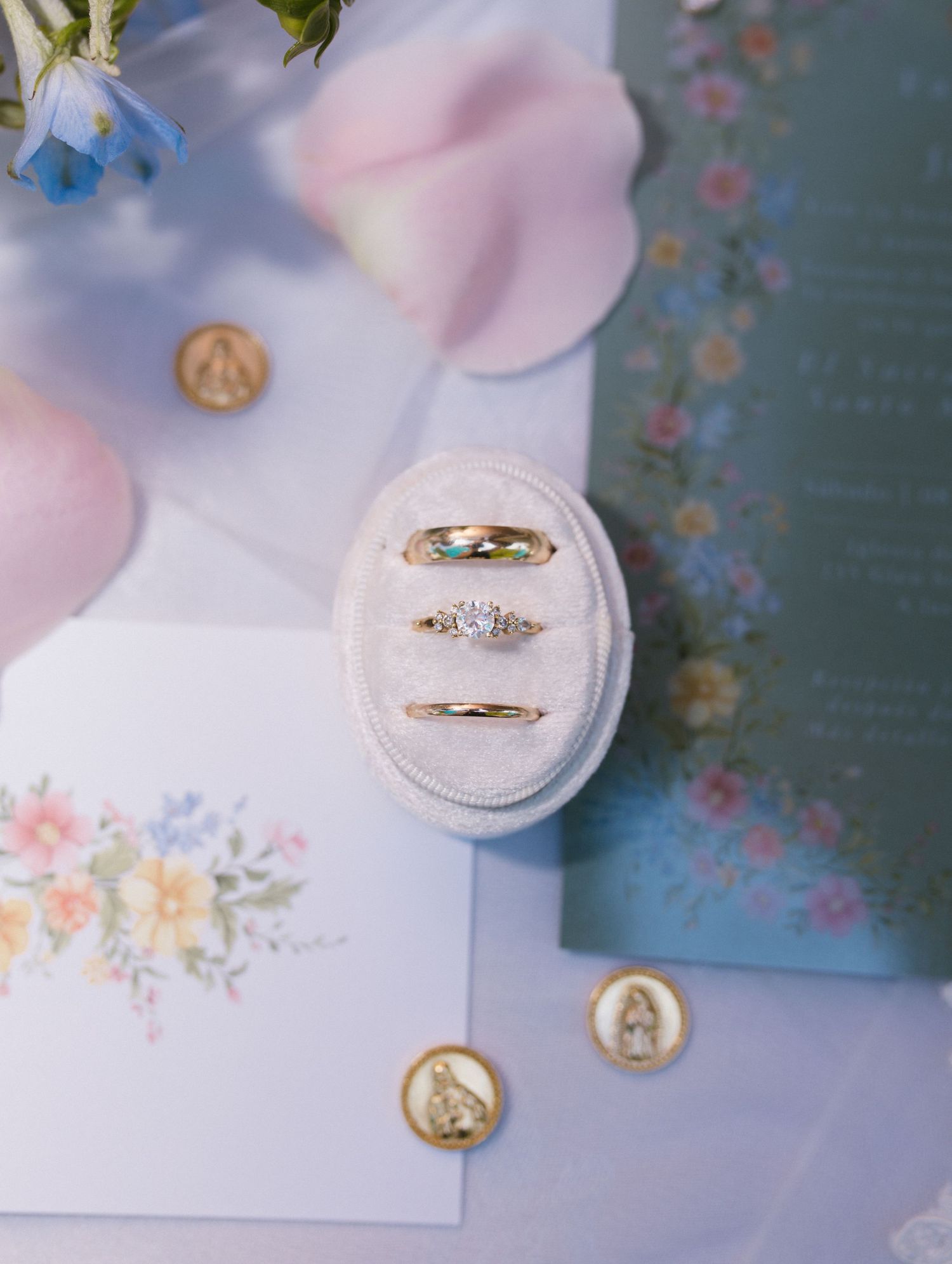 Three gold wedding rings displayed in oval velvet ring box with floral stationery and medallions.