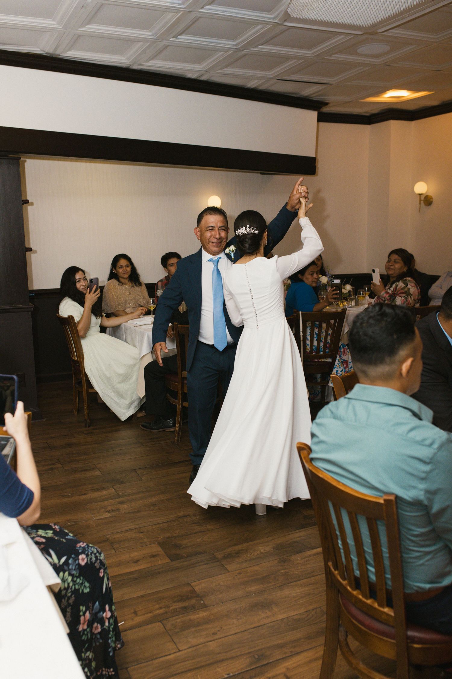 Bride and groom share first dance at wedding reception while guests watch and celebrate around them.