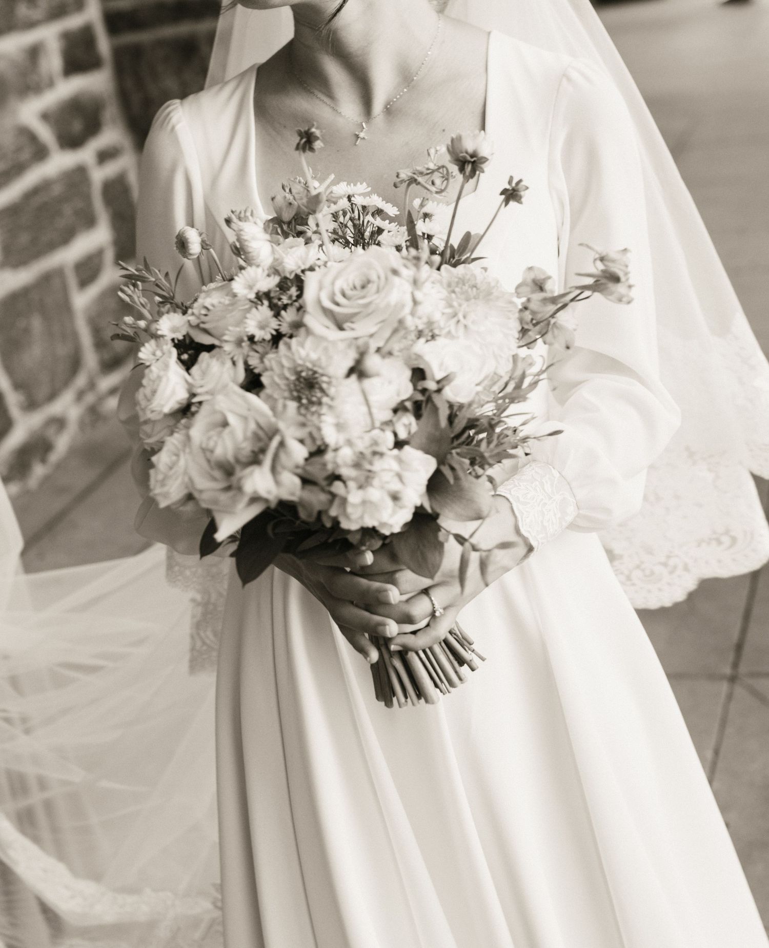 Bride in white gown holding elegant bouquet of roses and wildflowers, black and white wedding photography.