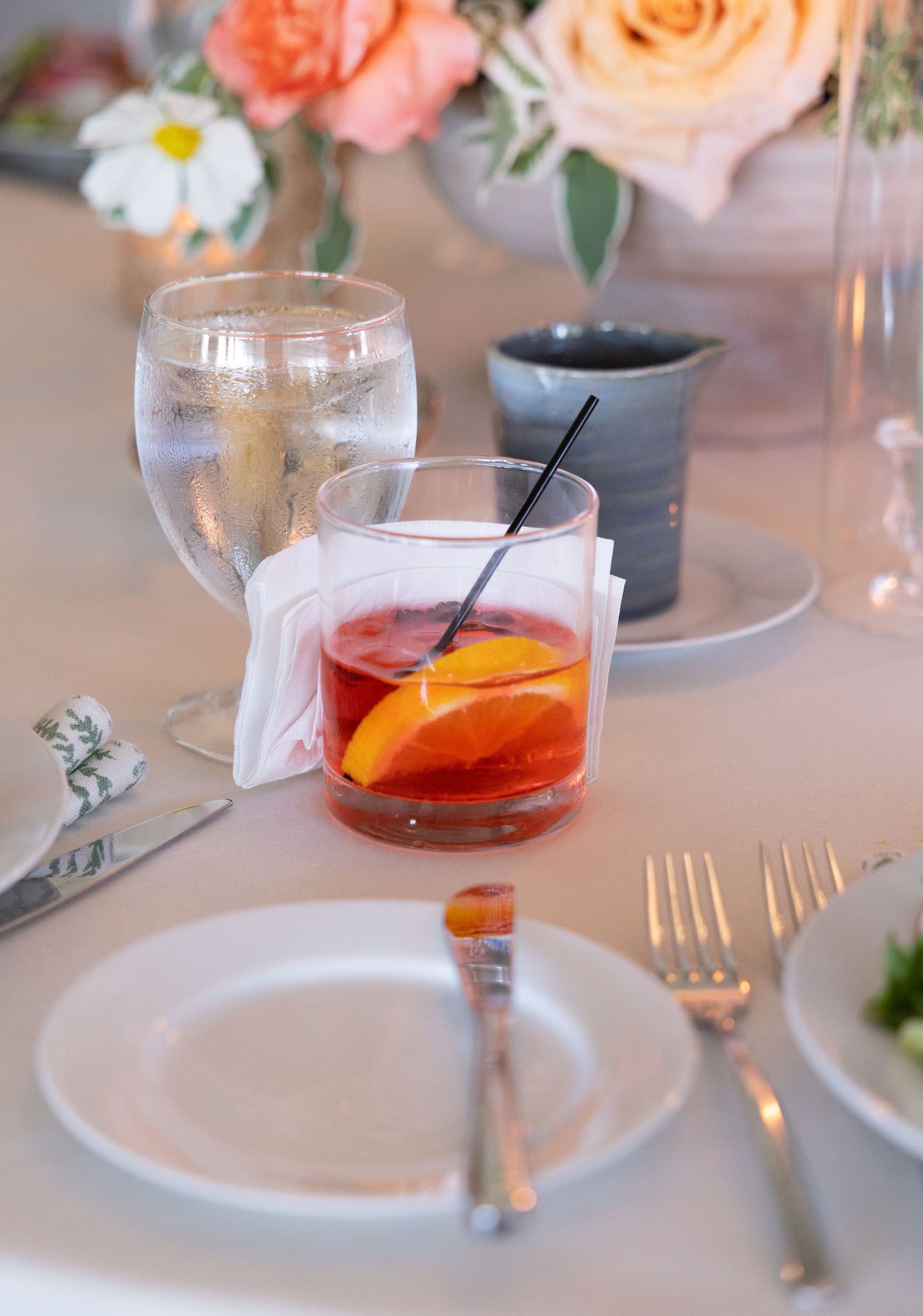 Wedding reception cocktail featuring an old fashioned drink with orange slice beside floral centerpiece.