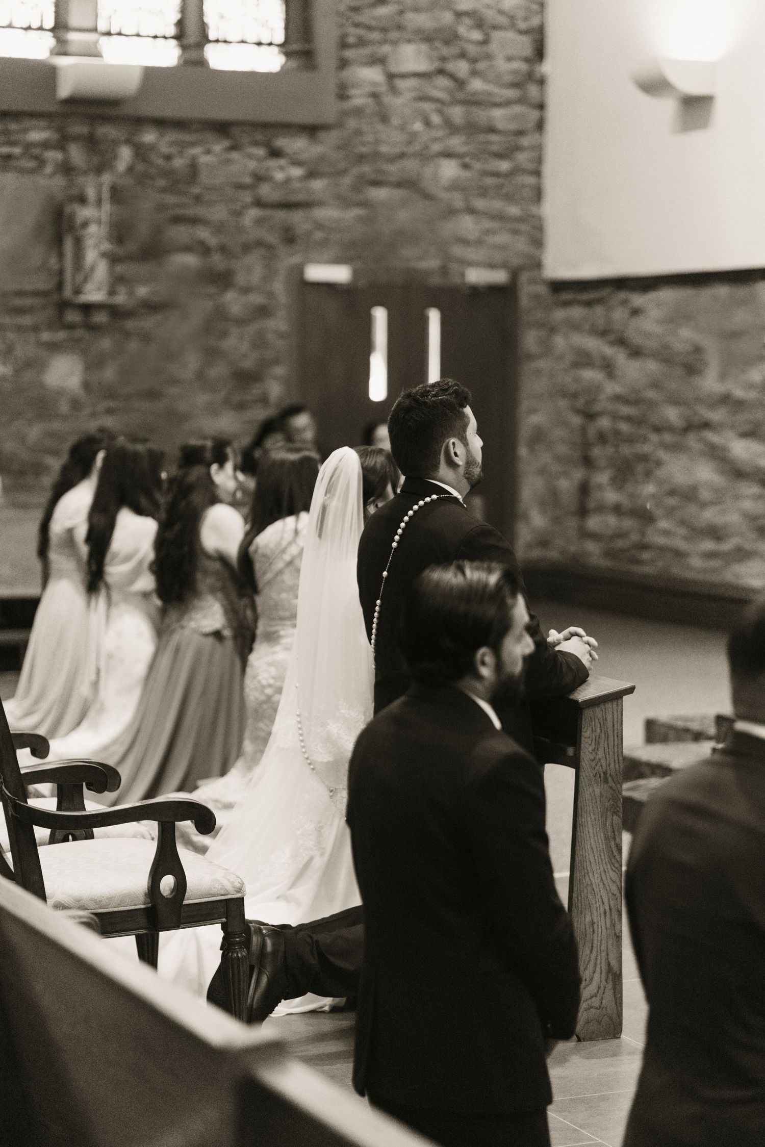 Black and white photo of bride and groom kneeling at church altar during wedding ceremony.