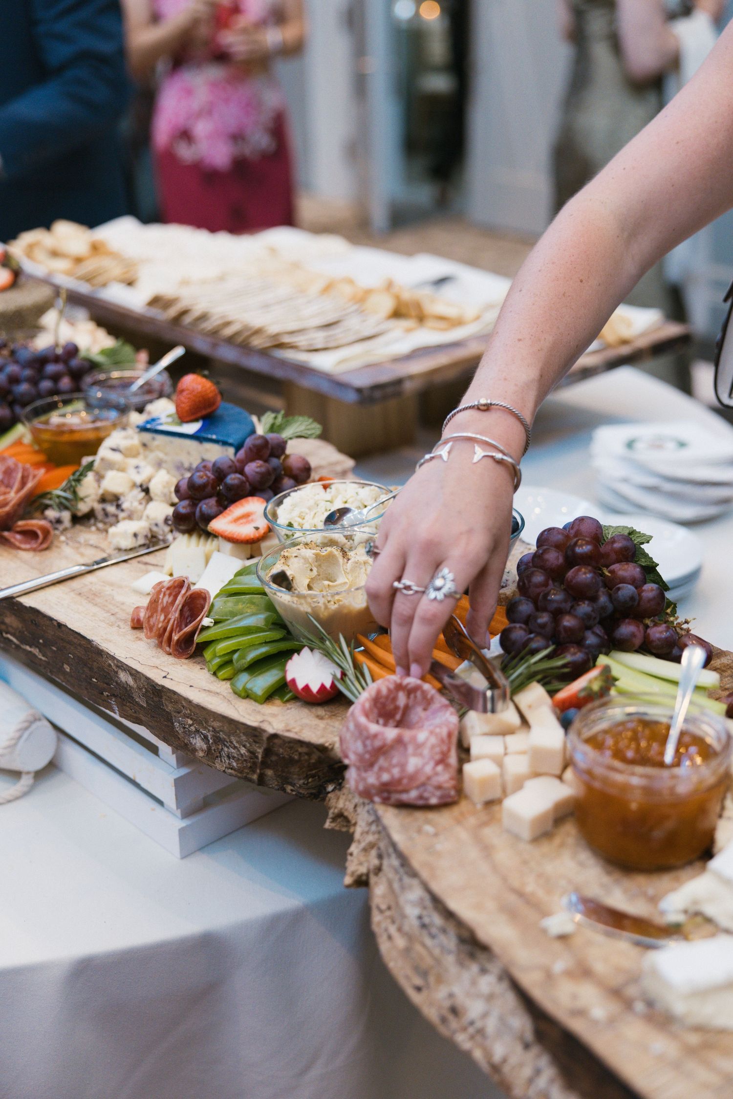 Guest reaching for charcuterie board with grapes, meats, and cheeses at wedding reception.