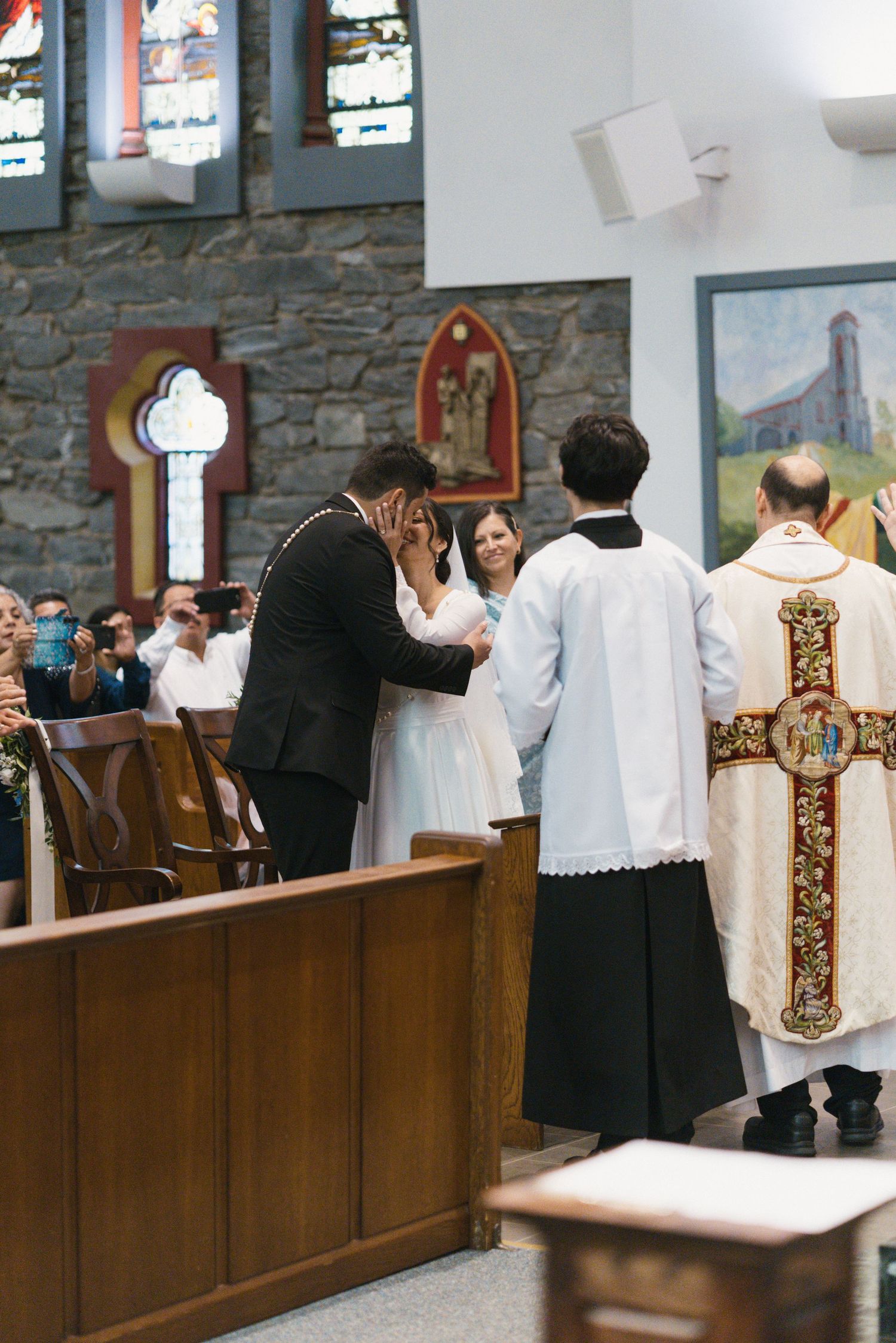 Couple exchanges vows at Catholic church ceremony with priest and altar server present.