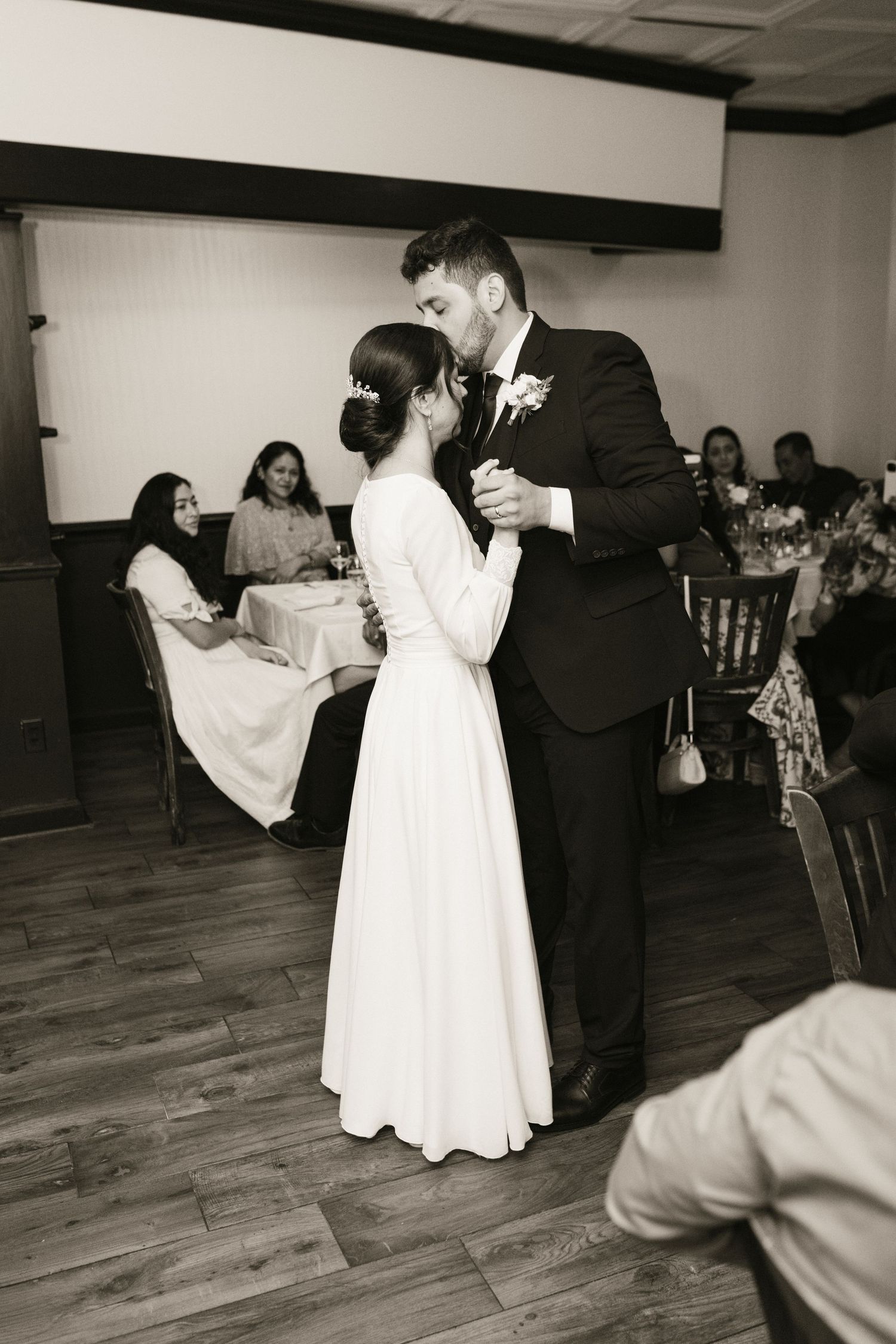 Bride and groom sharing first dance kiss in black and white wedding reception photo.