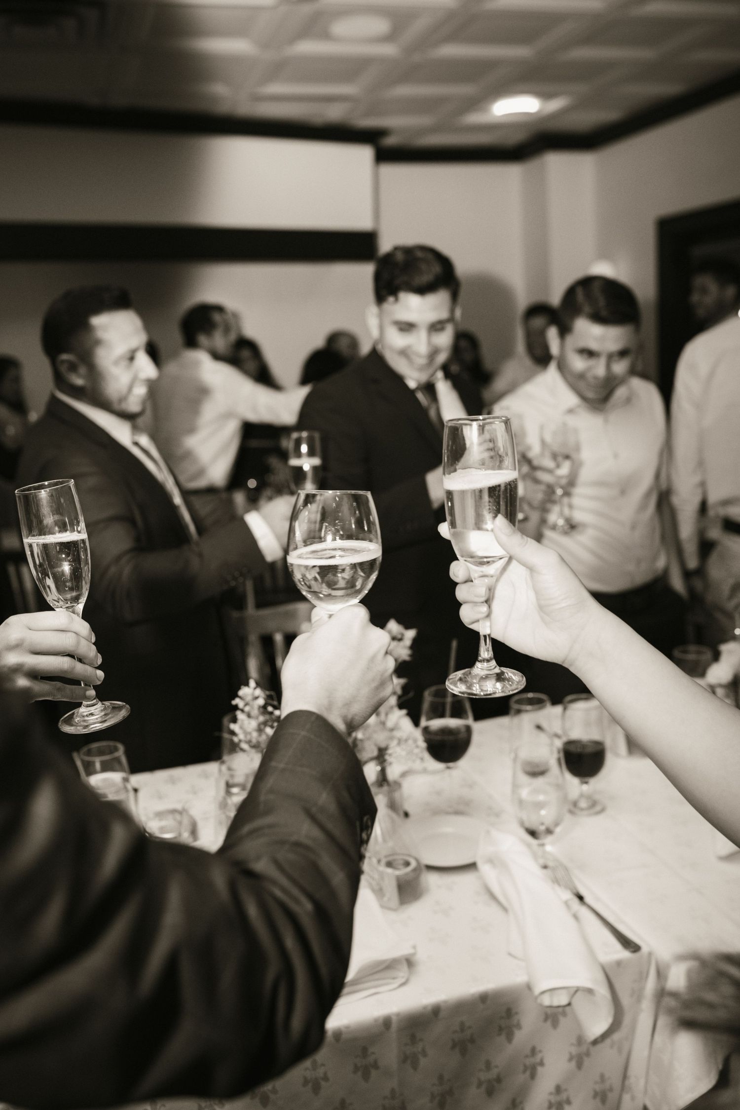 Wedding guests raising champagne glasses in a toast at the reception dinner celebration.