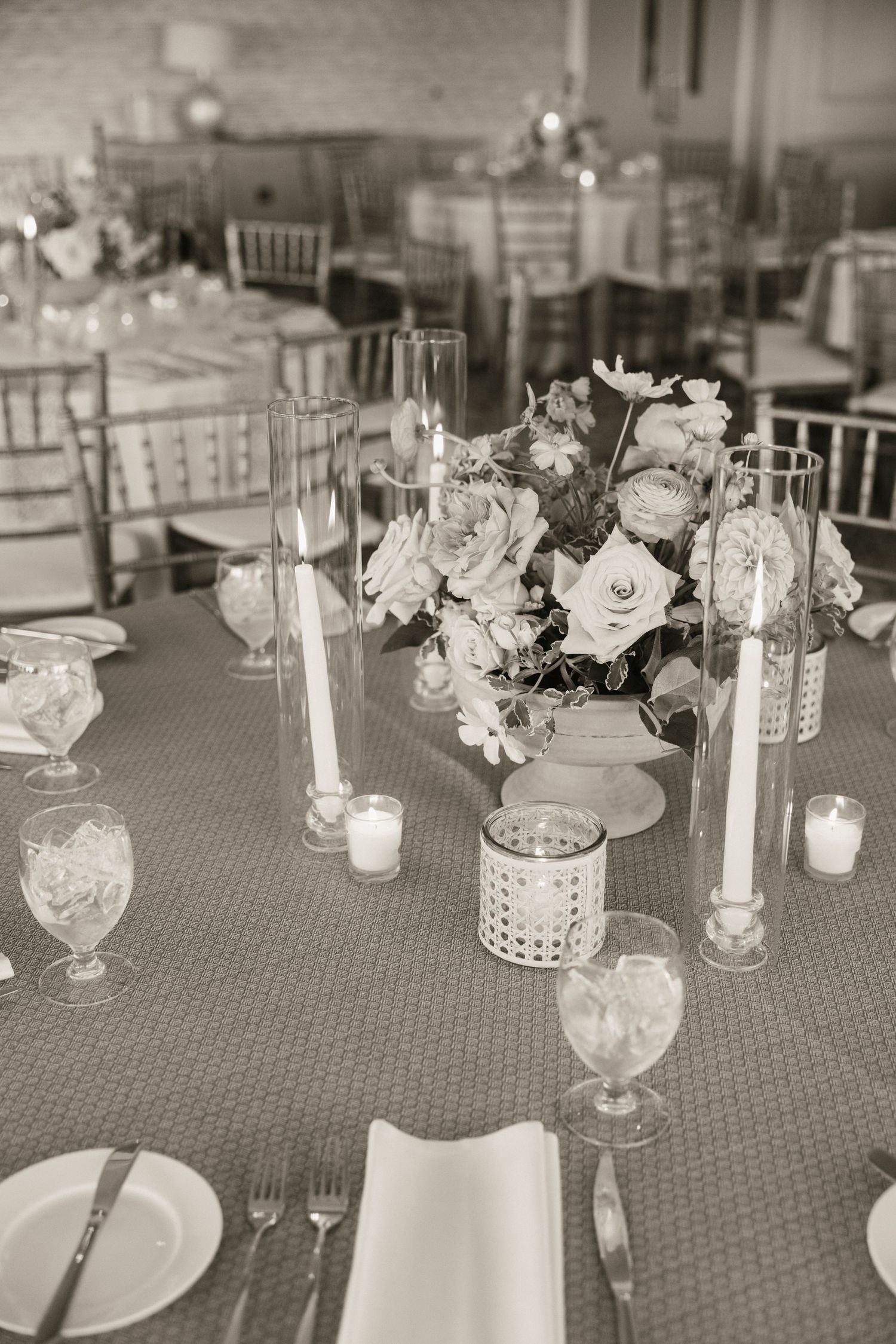 Black and white photo of wedding reception tables with floral centerpieces and candles.