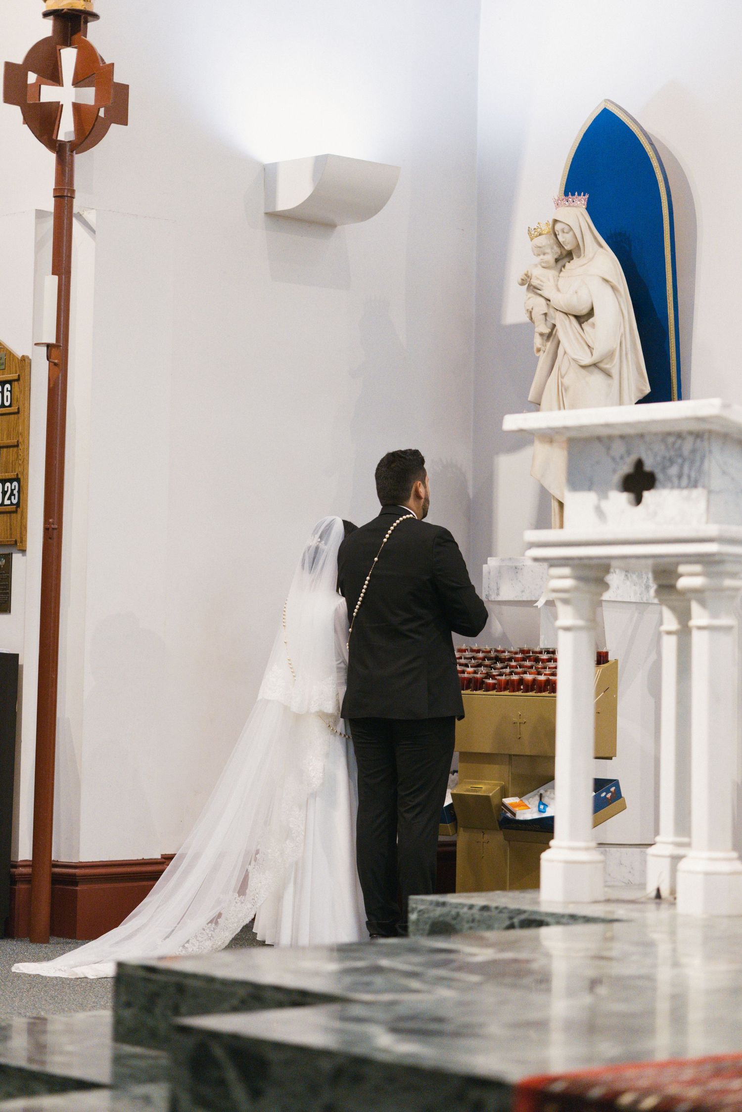 Bride and groom standing at church altar before a religious statue during wedding ceremony.