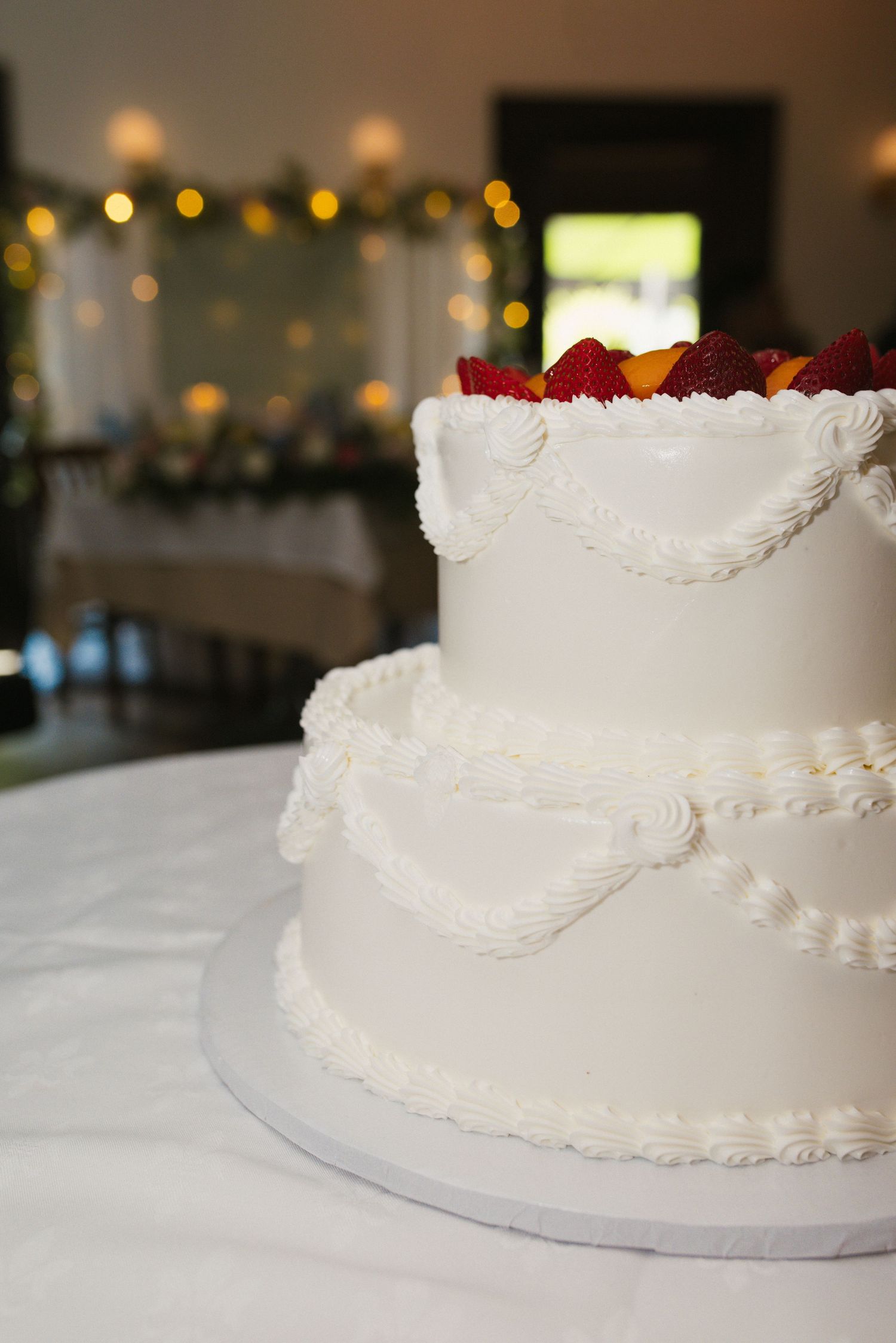Two-tier white wedding cake decorated with piped swags and fresh red and yellow fruit on top.
