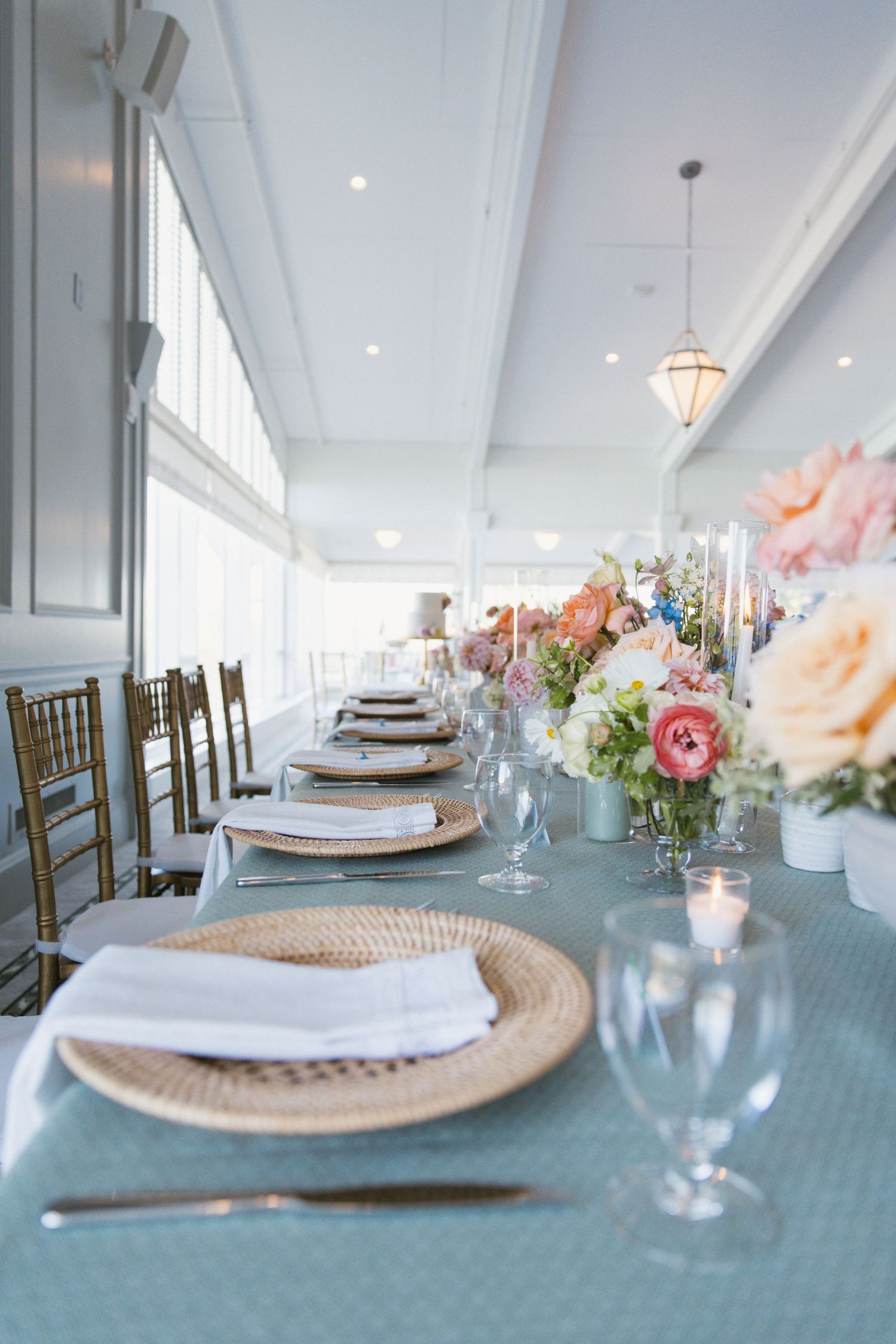 Elegant wedding reception table with woven chargers, blue linens, and pastel floral arrangements.