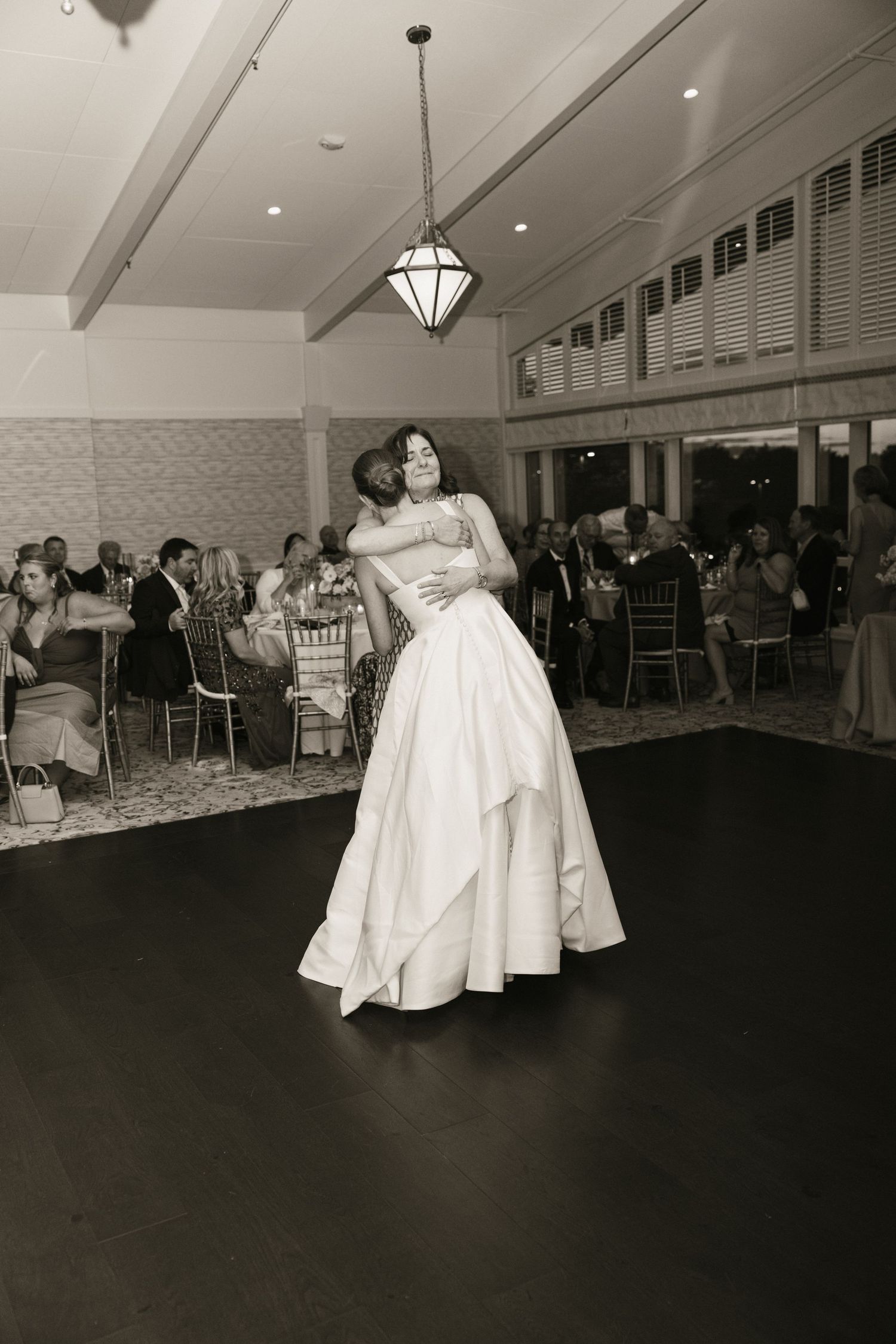 Black and white photo of groom lifting bride on wedding reception dance floor before cheering guests.