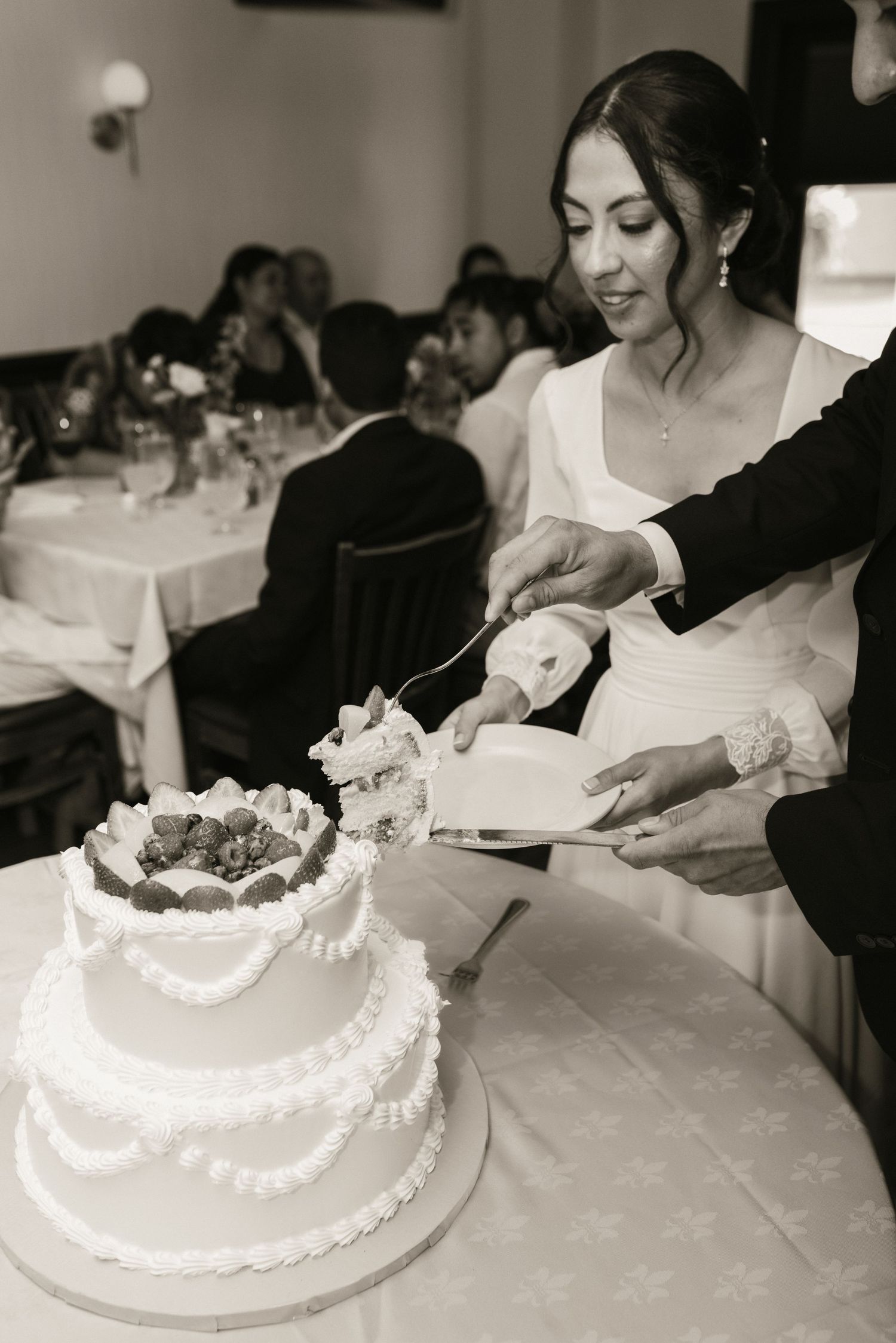 Bride and groom cutting white tiered wedding cake decorated with strawberries at reception.