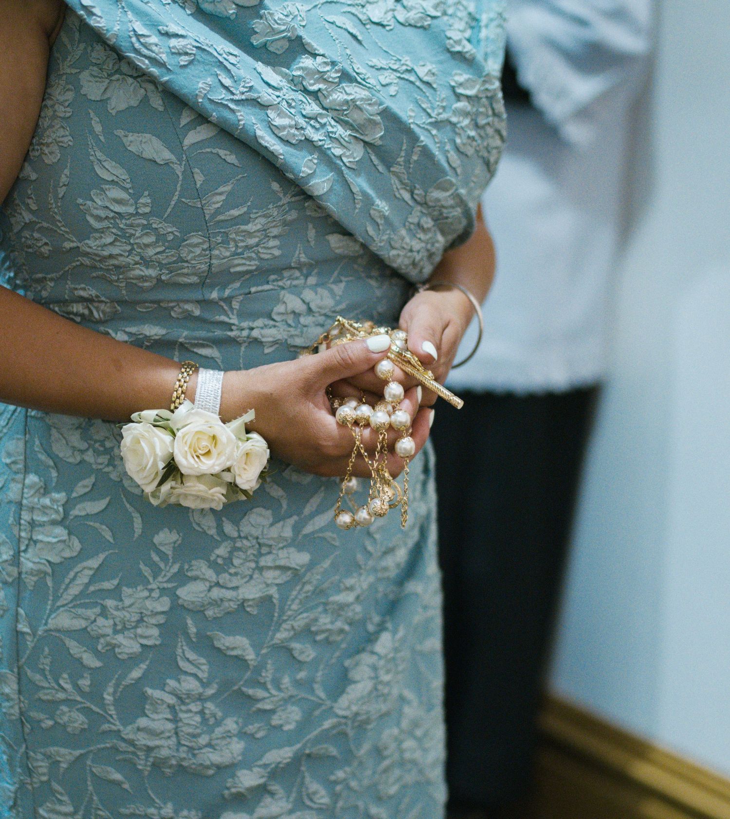 Close-up of woman in blue floral sari wearing pearl bracelets and white rose wrist corsage at formal event.