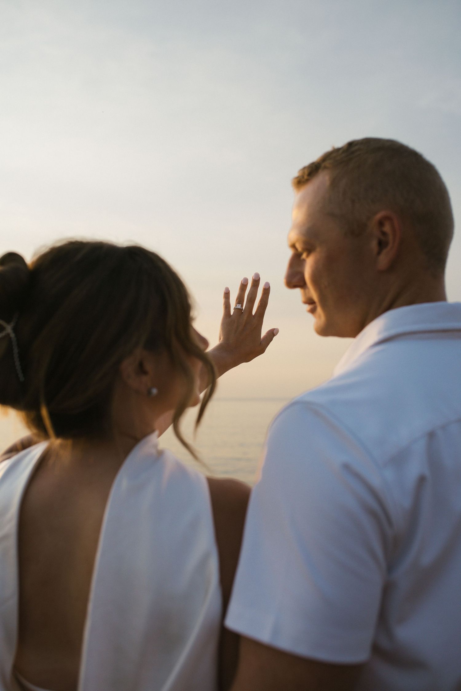 Close-up of engaged woman showing her ring to partner during romantic sunset session.