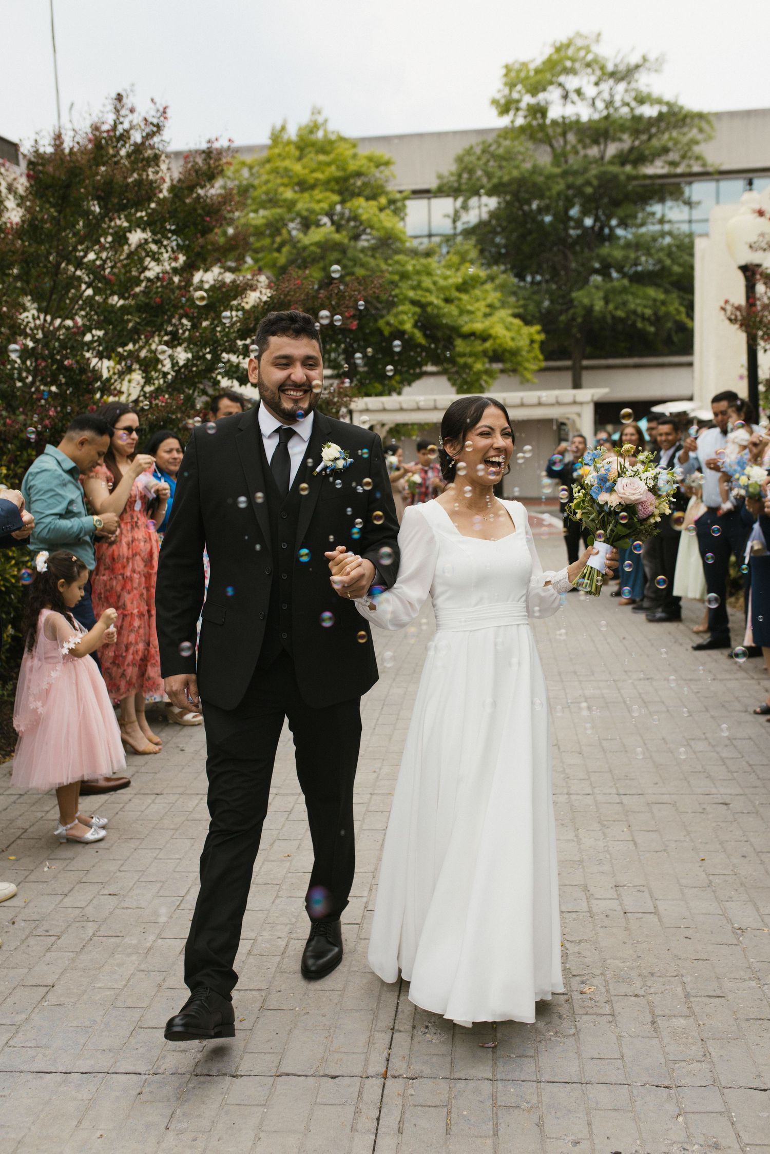 Joyful newlyweds walk through bubble send-off surrounded by cheering guests after outdoor ceremony.