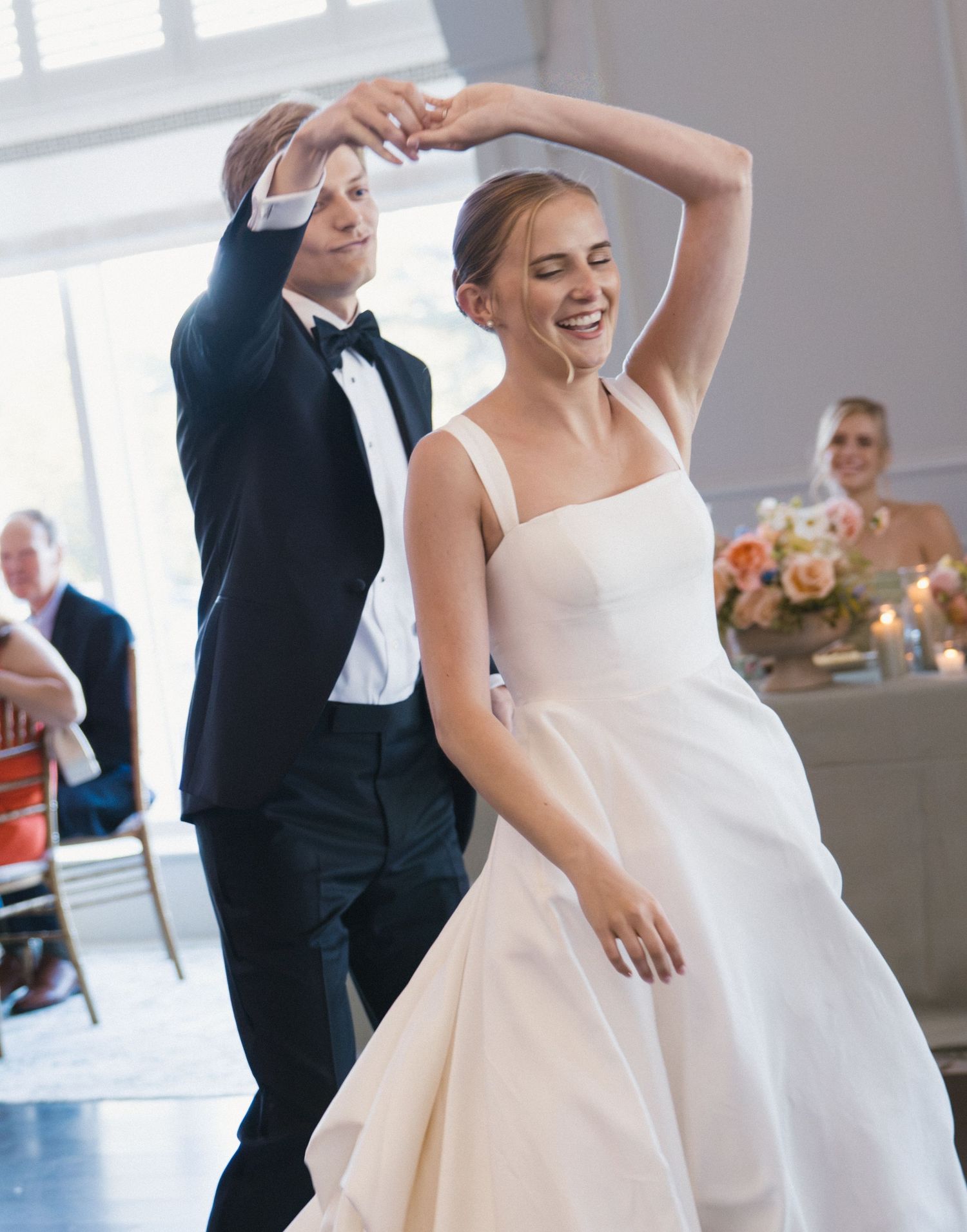 Bride and groom share a joyful first dance, groom spinning bride in a classic white ballgown at their wedding reception.