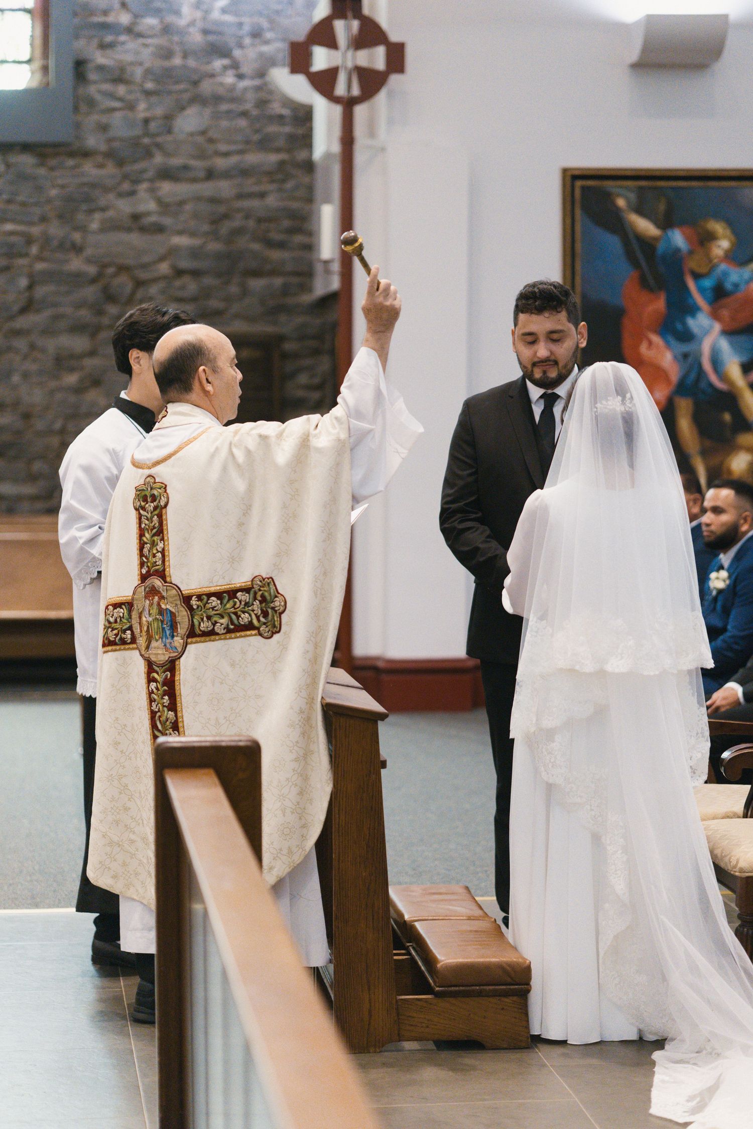 Priest blessing bride and groom kneeling at the altar during a Catholic wedding ceremony.