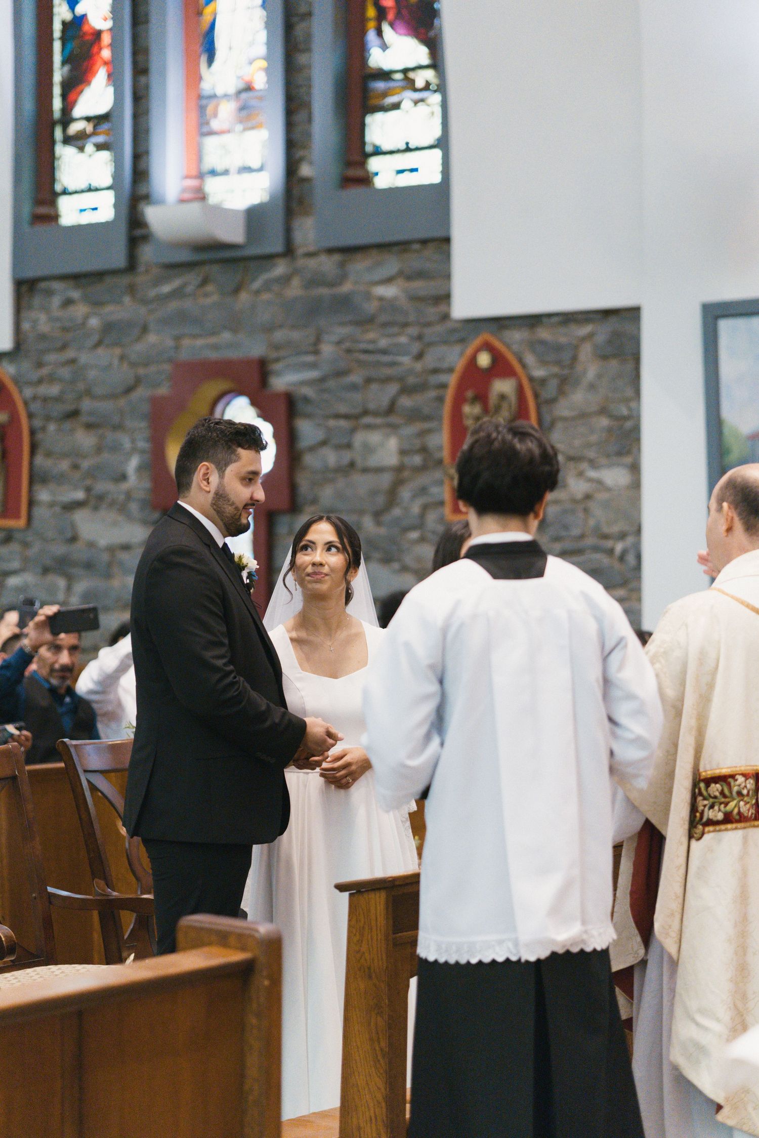 Bride and groom exchange vows at the altar of a stone Catholic church during their wedding ceremony.