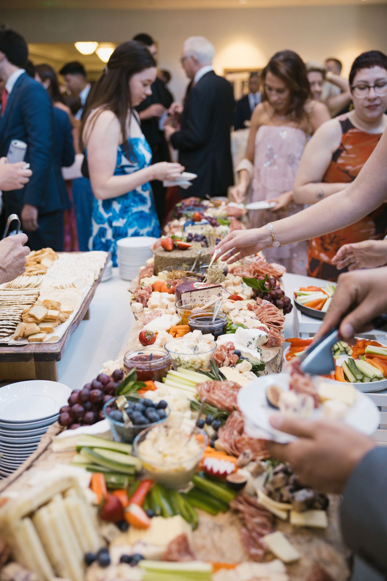 Wedding guests enjoy an elaborate charcuterie and appetizer spread at a elegant reception cocktail hour buffet table.