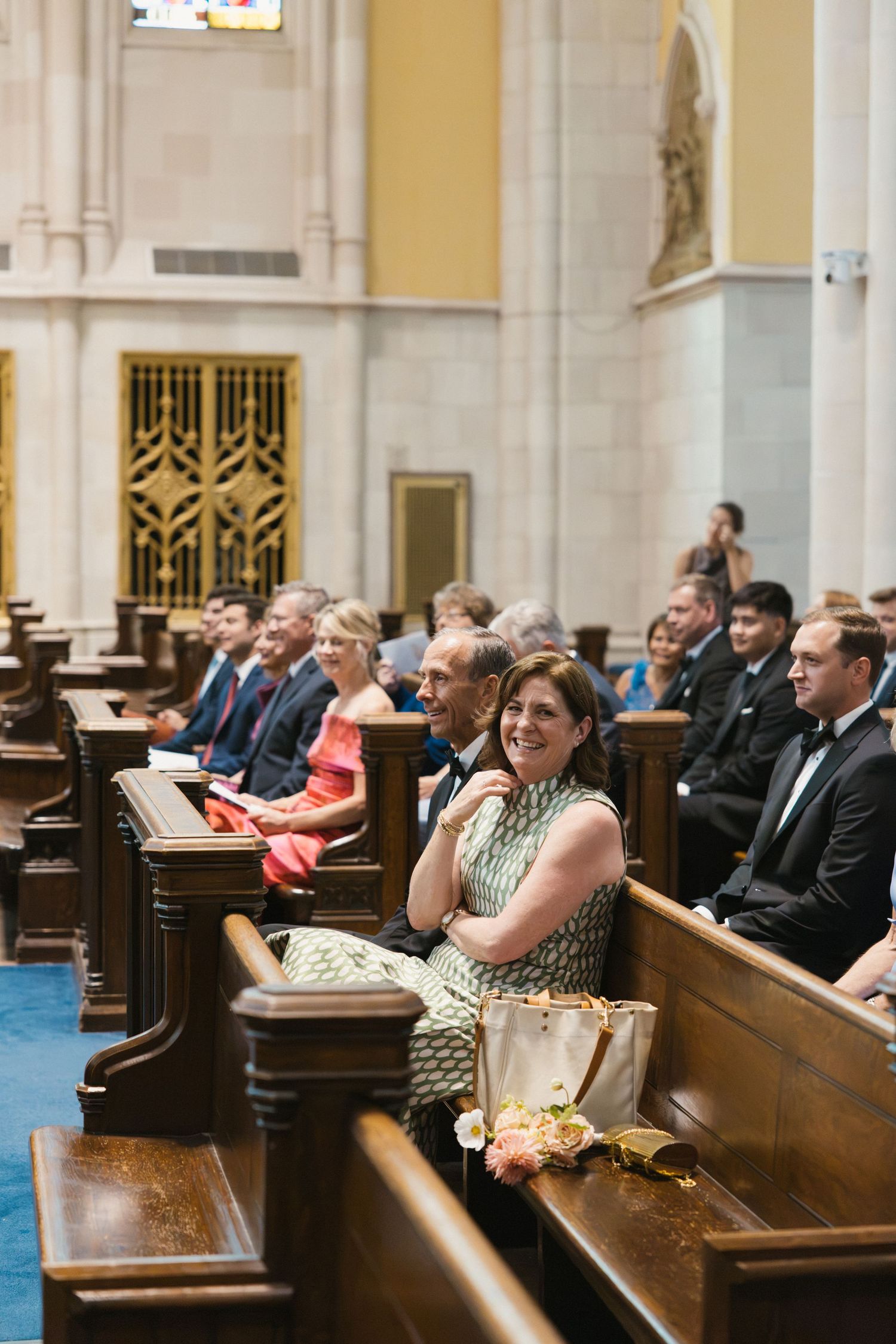 Wedding guests seated in ornate church pews smiling during a formal ceremony.