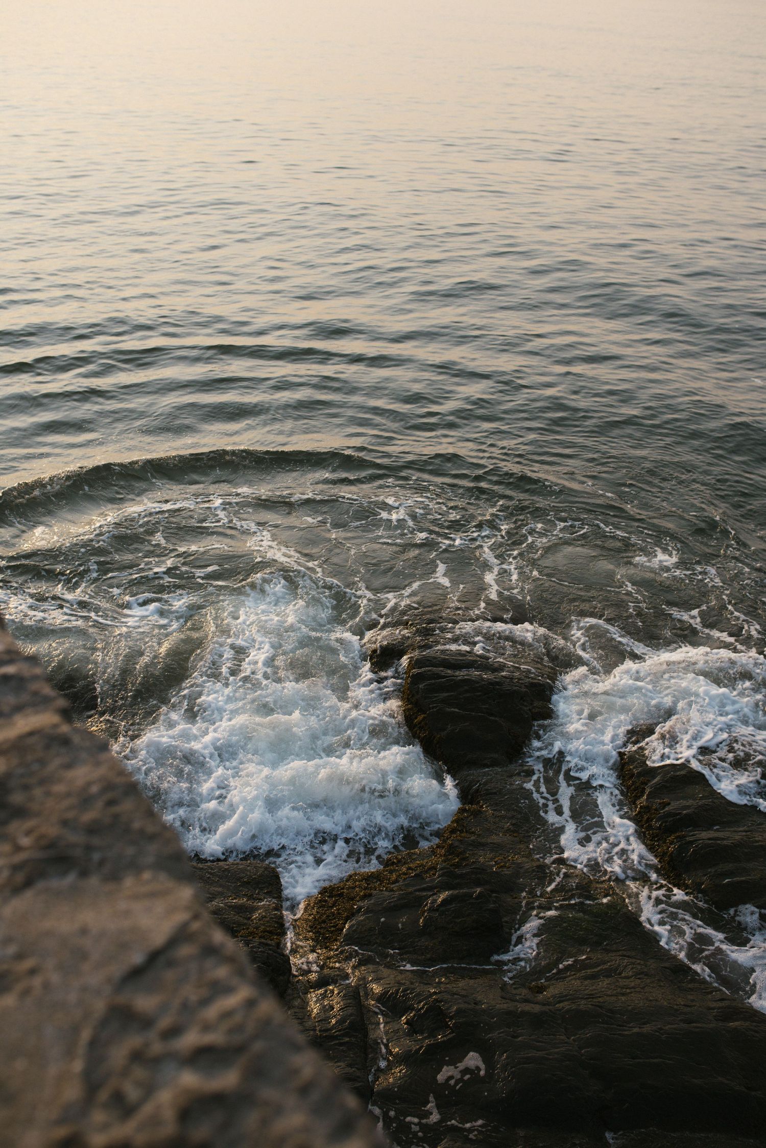 Ocean waves crashing against rocky shoreline in soft evening light.