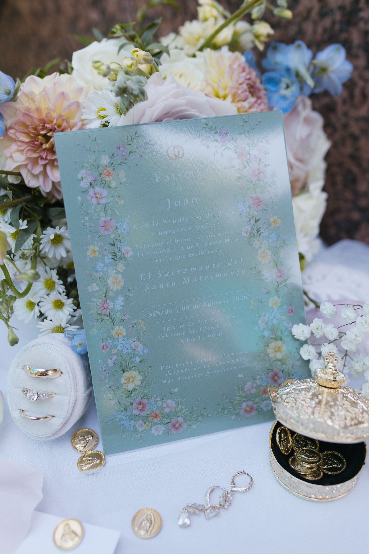Elegant floral wedding invitation in mint green displayed with rings and jewelry accessories.