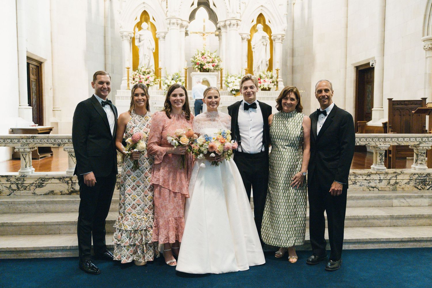 Wedding party poses together inside an elegant church with blue carpet and ornate golden altar decorations.