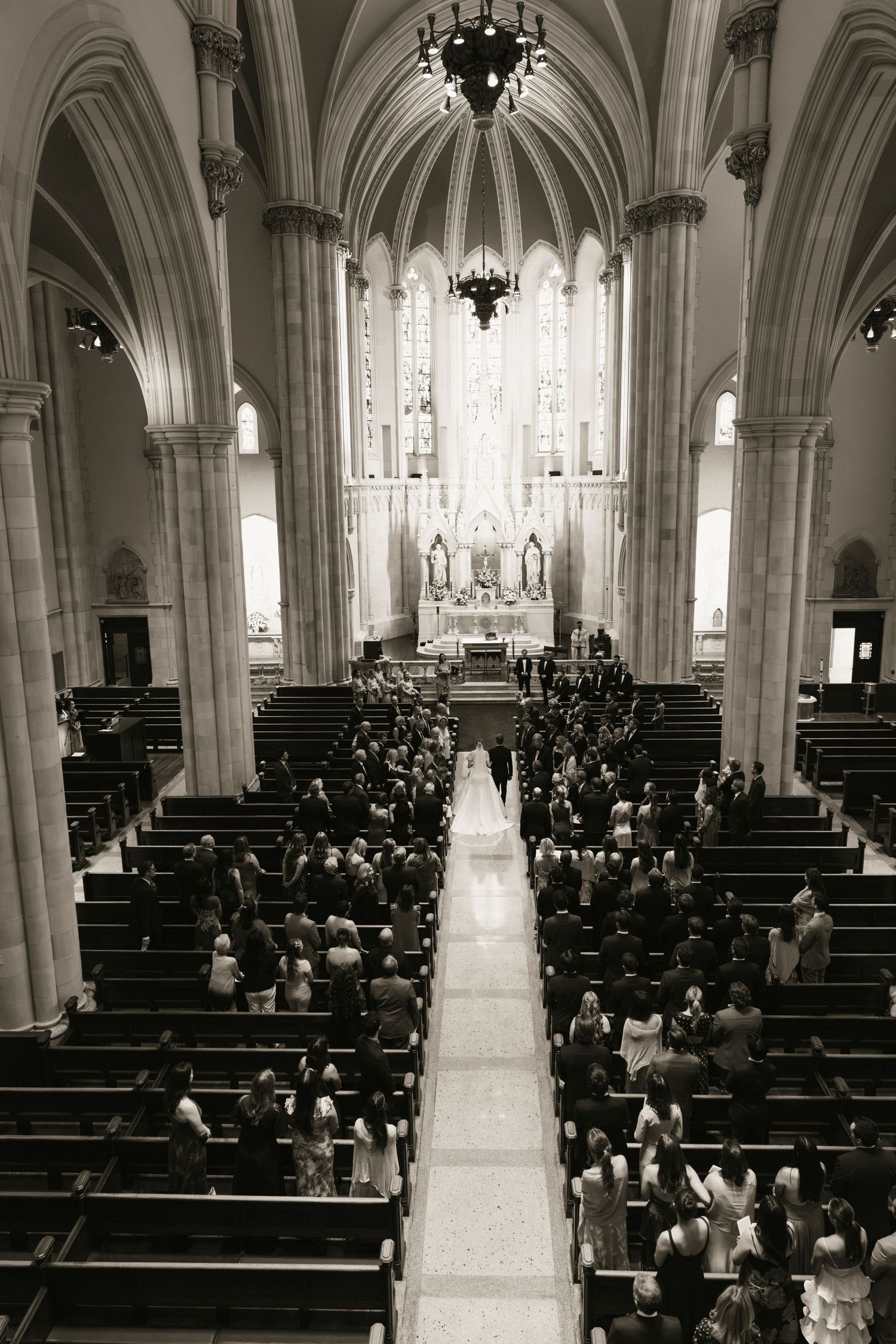 Black and white aerial view of a wedding ceremony inside a grand Gothic church with ornate arches and stained glass.