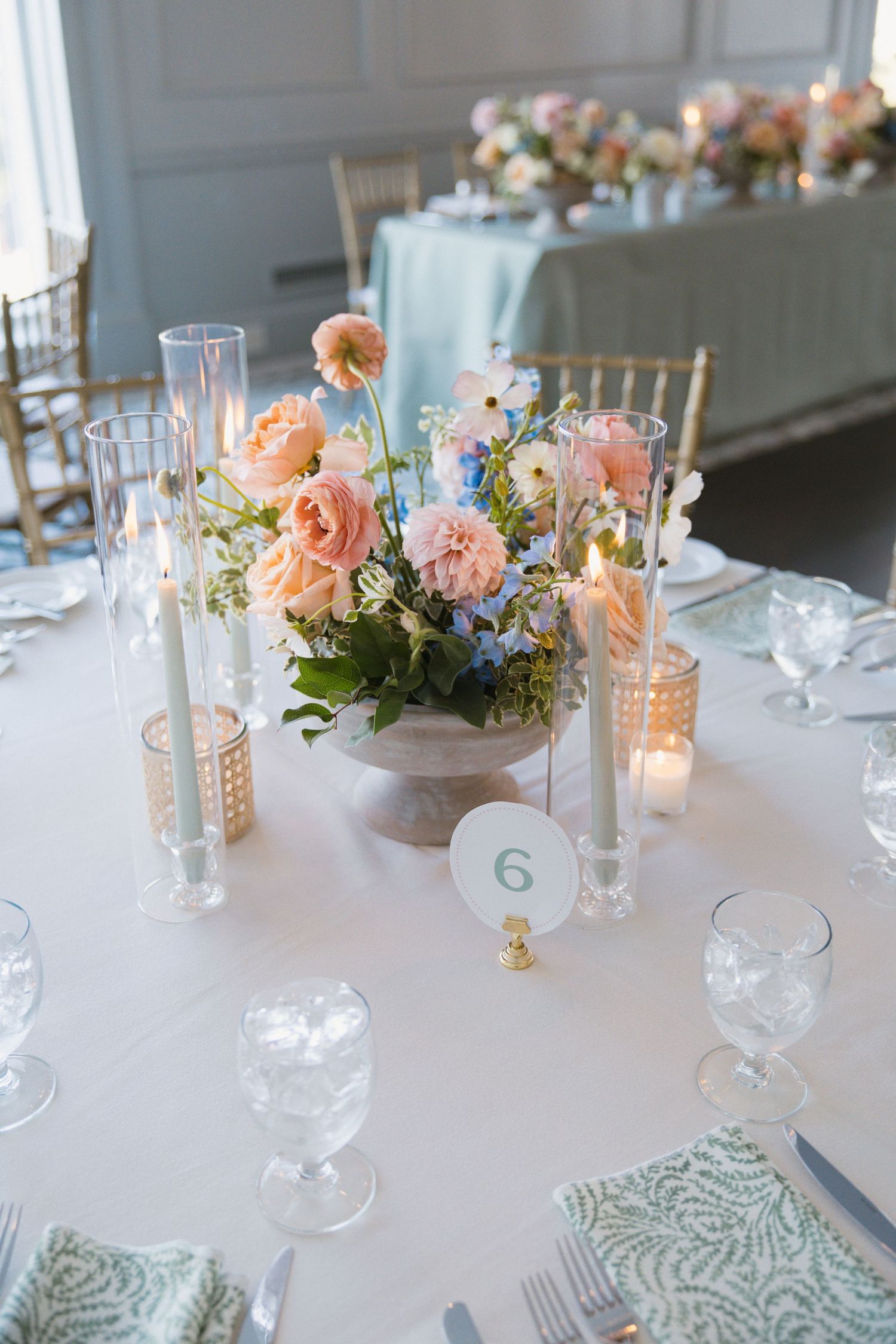 Round wedding reception table with peach and pink floral centerpiece, taper candles, and green patterned napkins.