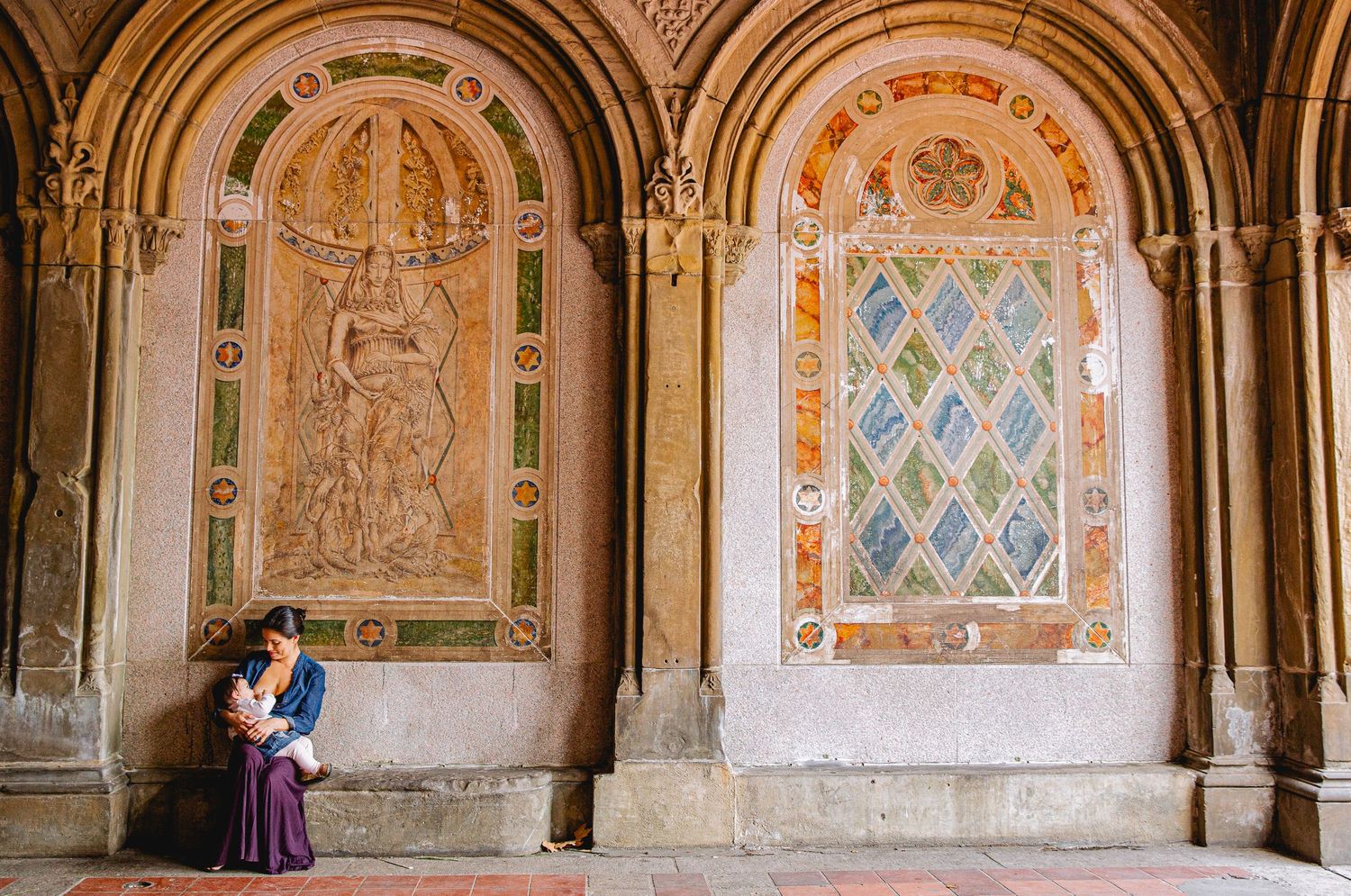 Couple sitting beneath ornate arched walls with colorful tilework and relief sculptures at Bethesda Terrace, Central Park.